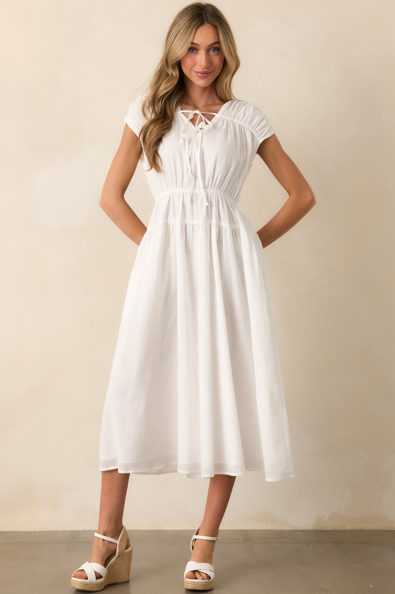 A charming ivory dress with a v-neckline and optional self-tie bows, short cap sleeves, an elastic waist for comfort, and functional pockets for convenience.