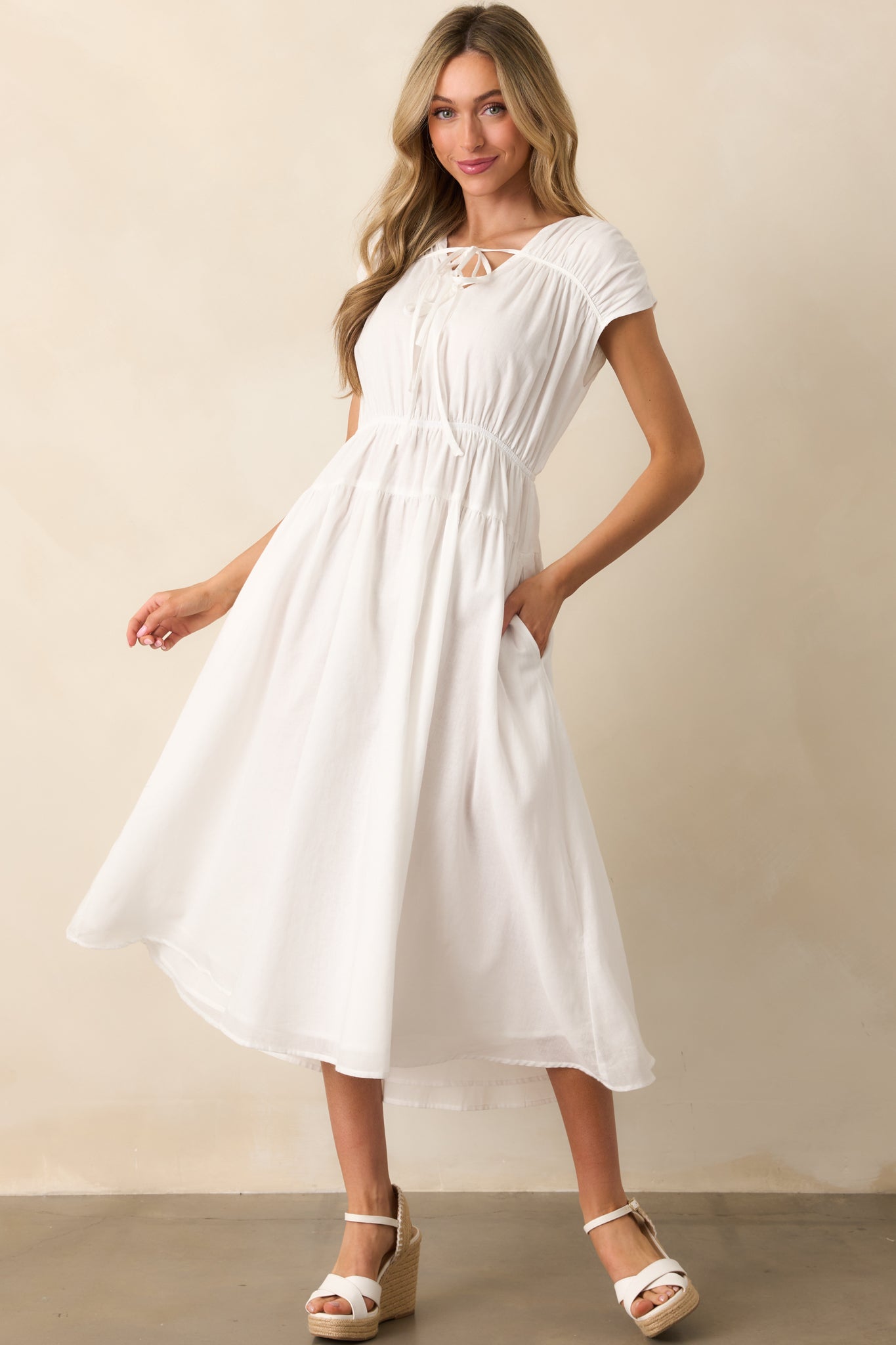 An ivory dress with a flattering v-neckline, optional self-tie bows, short cap sleeves, an elastic waist, and functional pockets for a relaxed, feminine look.