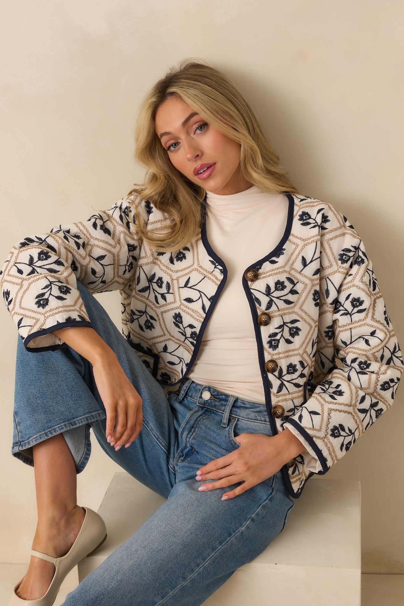 Close-up of tortoise shell button front closure and floral geometric embroidery on ivory fabric.