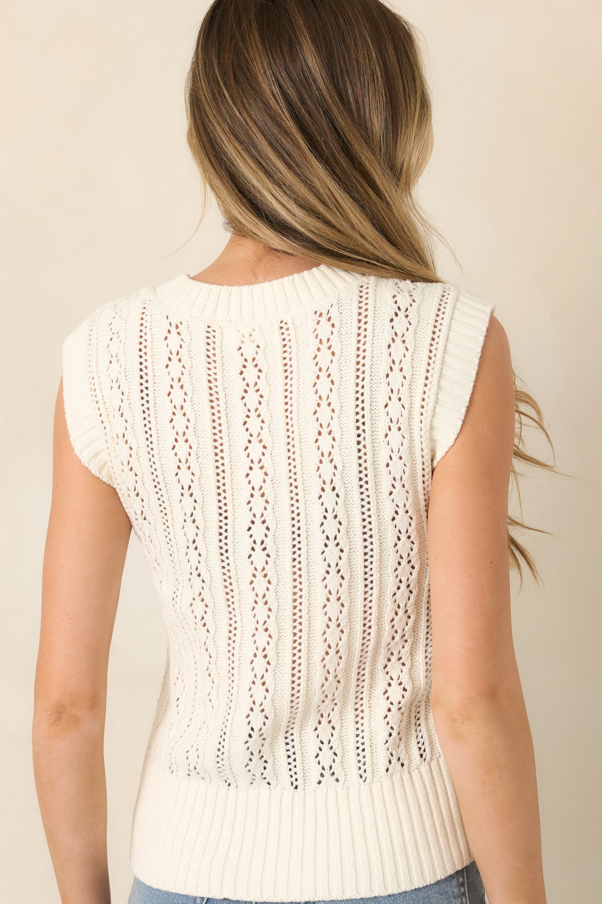 Rear of ivory fitted vest showcasing textured knit patterns and ribbed hem.