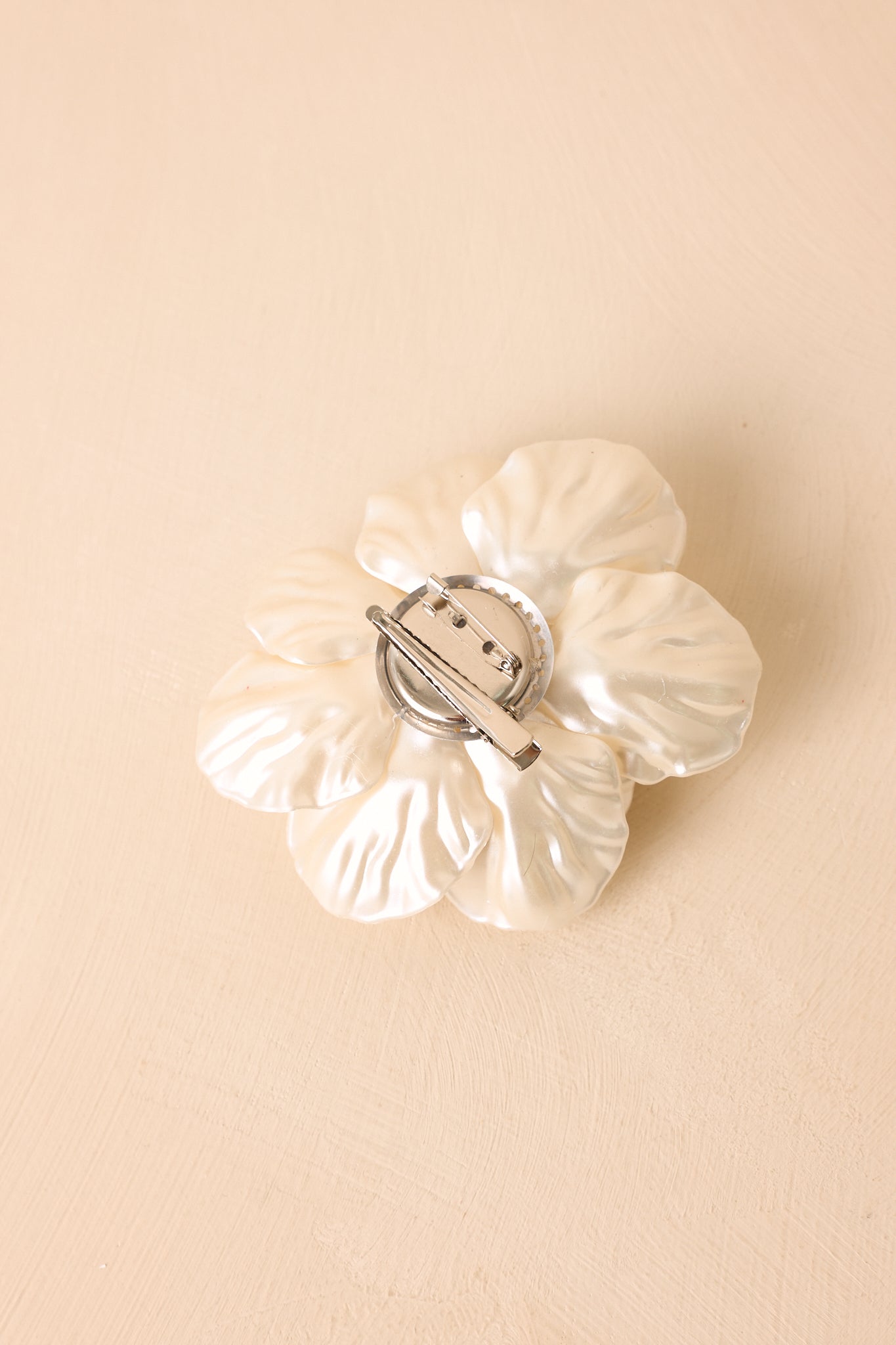 Back view of the ivory floral accessory showing the barrette clip and safety pin backing.