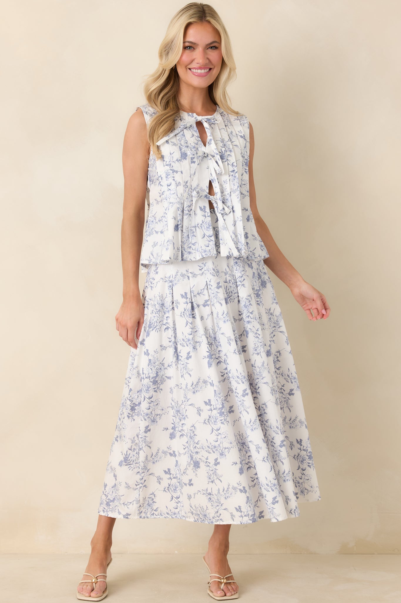 Ivory sleeveless top with delicate blue floral print, adjustable front bows, and a gentle swing-style shape.