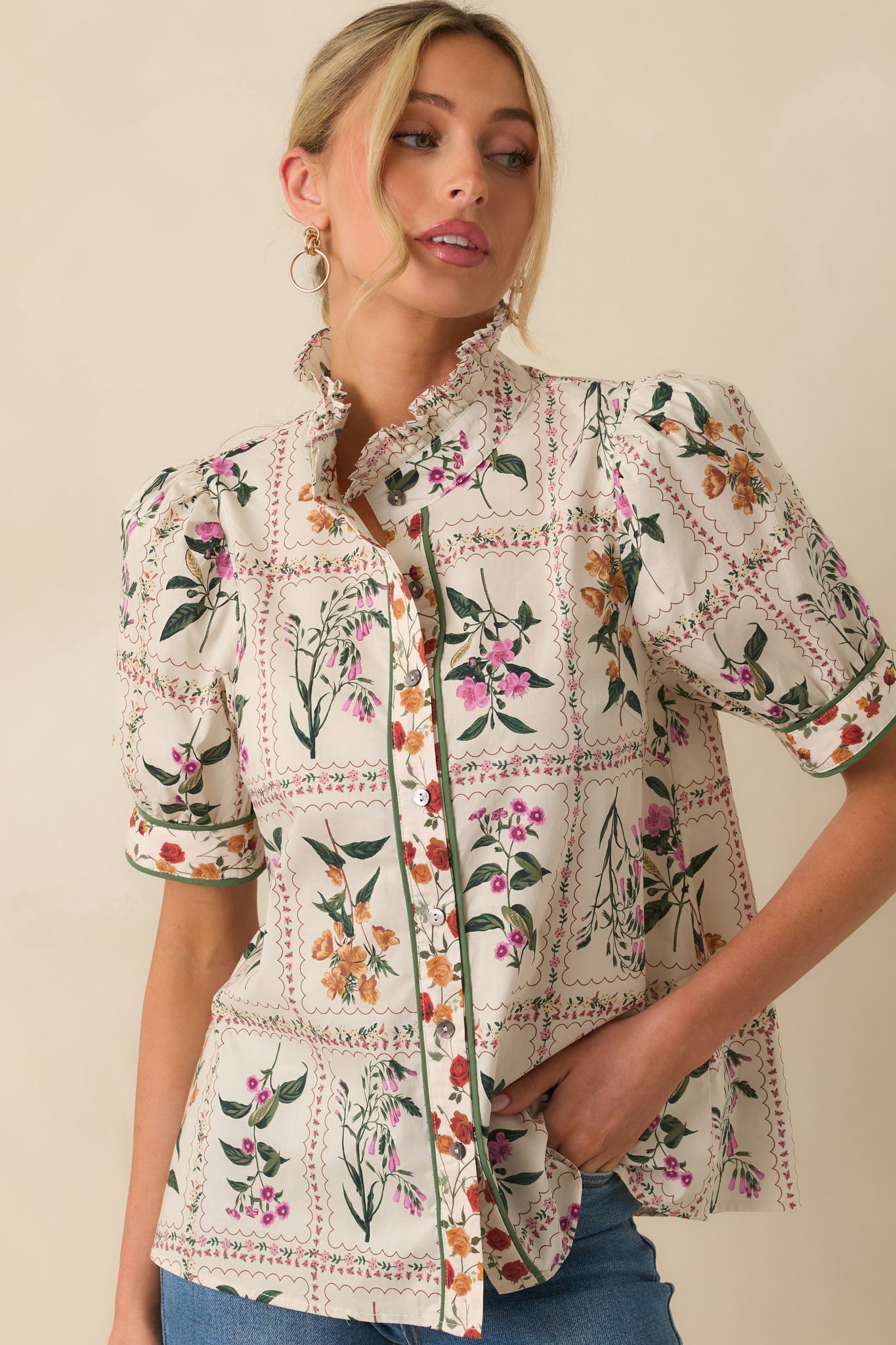 A cropped front view focusing on the ruffle collar and button closure of the ivory floral top.