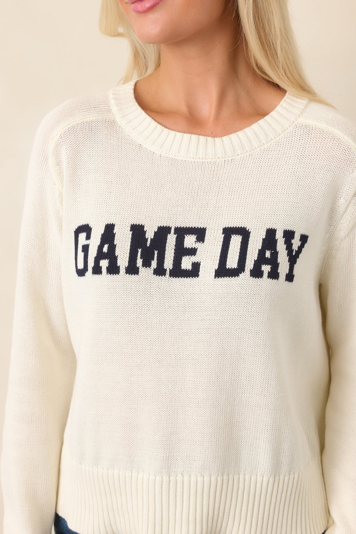 Close-up of the ivory knit top highlighting the bold navy “GAME DAY” lettering and textured ribbed trim around the neckline.