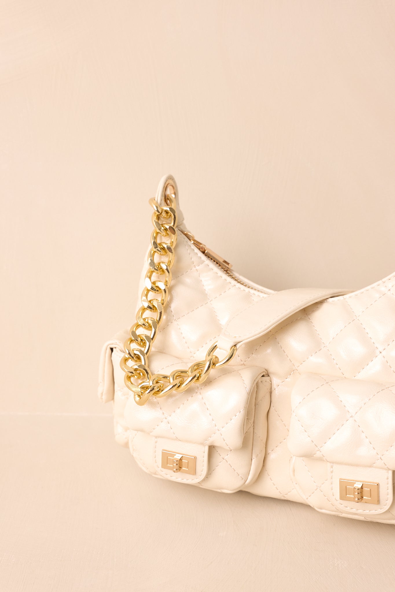 A close-up detail of the ivory handbag highlighting the gold turn-lock hardware, quilted stitching, and smooth finish.
