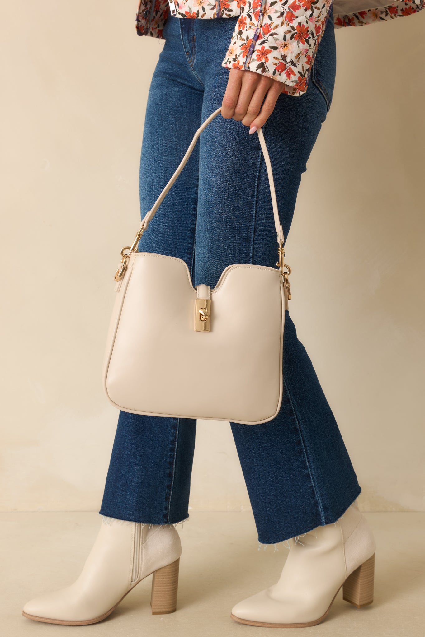 Ivory handbag featuring gold turn lock closure, gold hardware, and sleek structured silhouette.