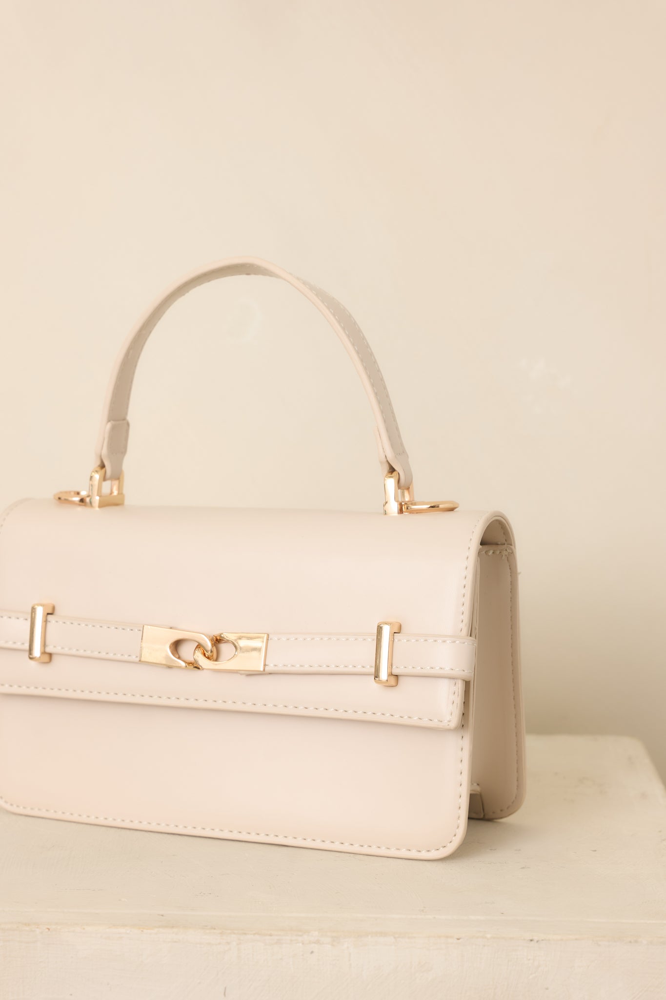 Close-up of the ivory handbag revealing the elegant front belt detail, interlocking accent, and polished gold-tone hardware.