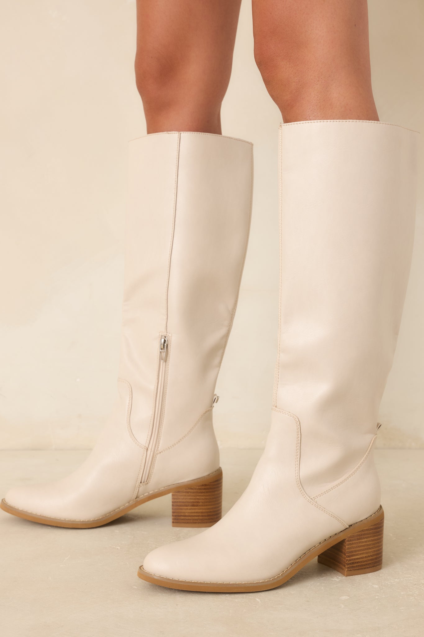 Detailed view of ivory knee-high boots featuring Western-inspired seaming, sleek material finish, and structured shaft design.