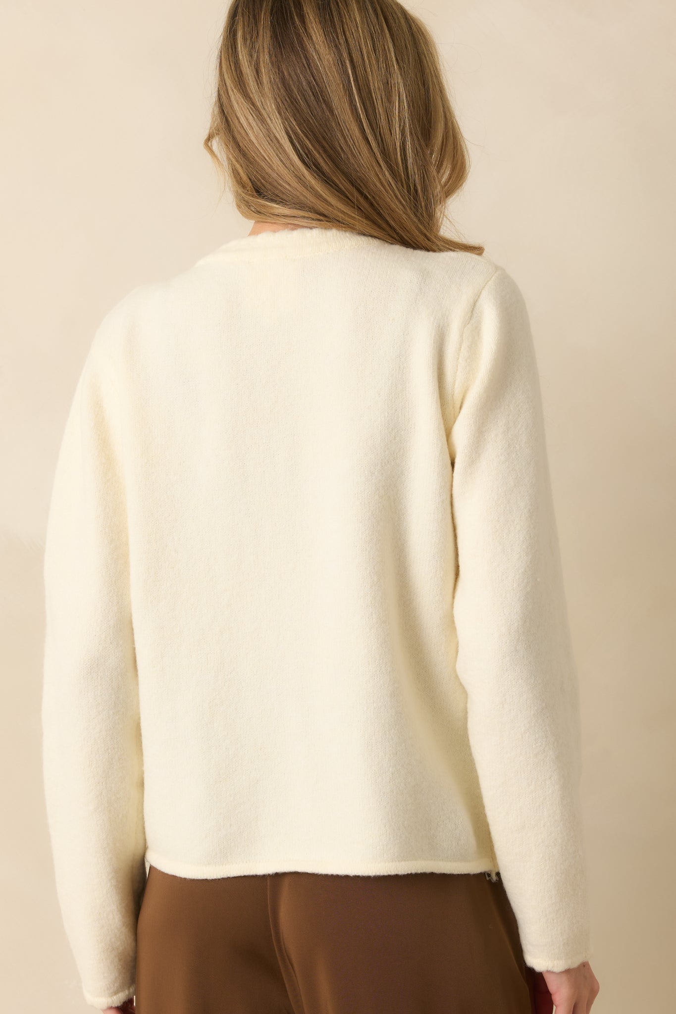 A back view of the ivory cardigan featuring a soft knit material, scalloped hem, and long sleeves.