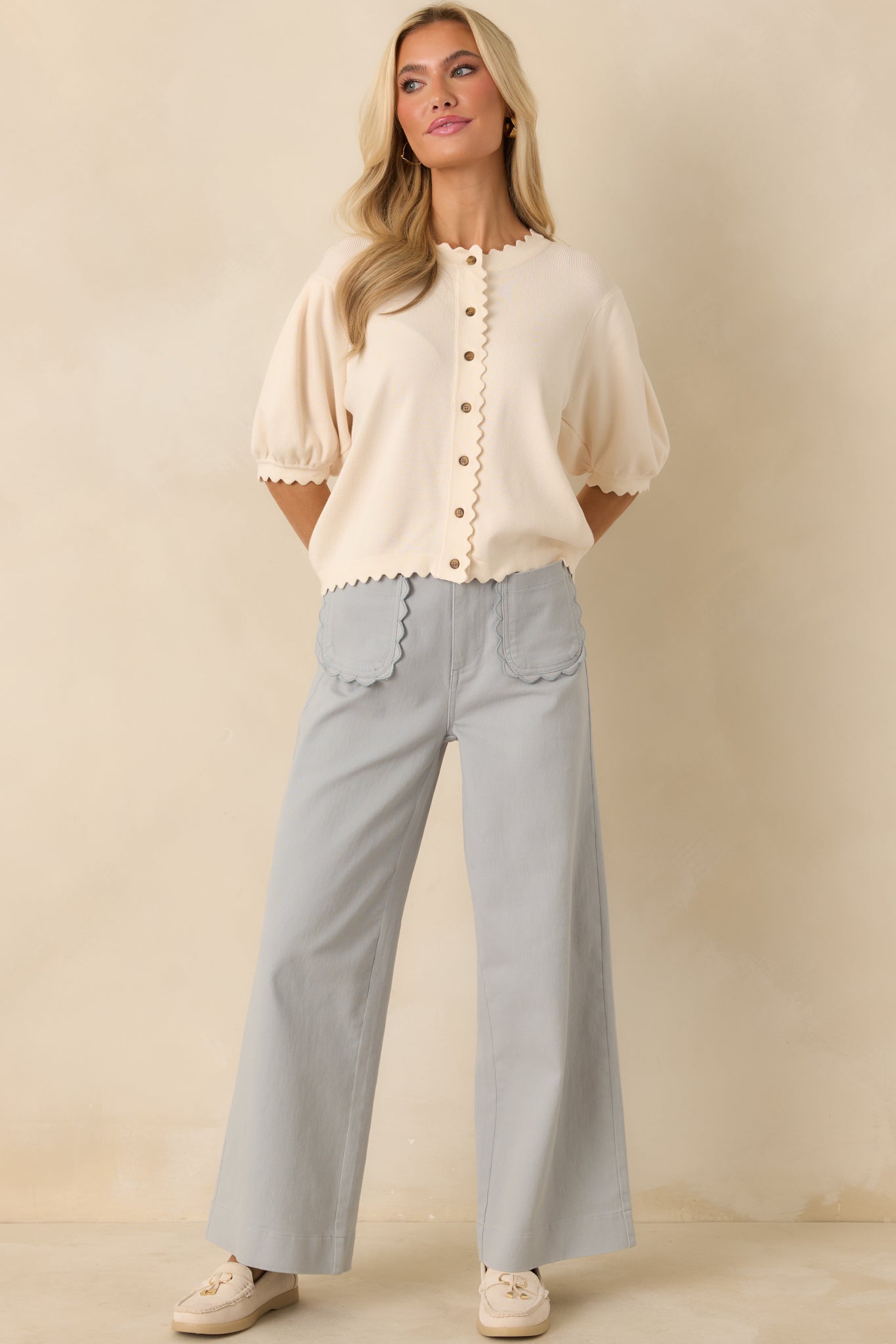 Creamy ivory knit cardigan designed with a structured button front, puff sleeves, and delicate scalloped trim throughout.