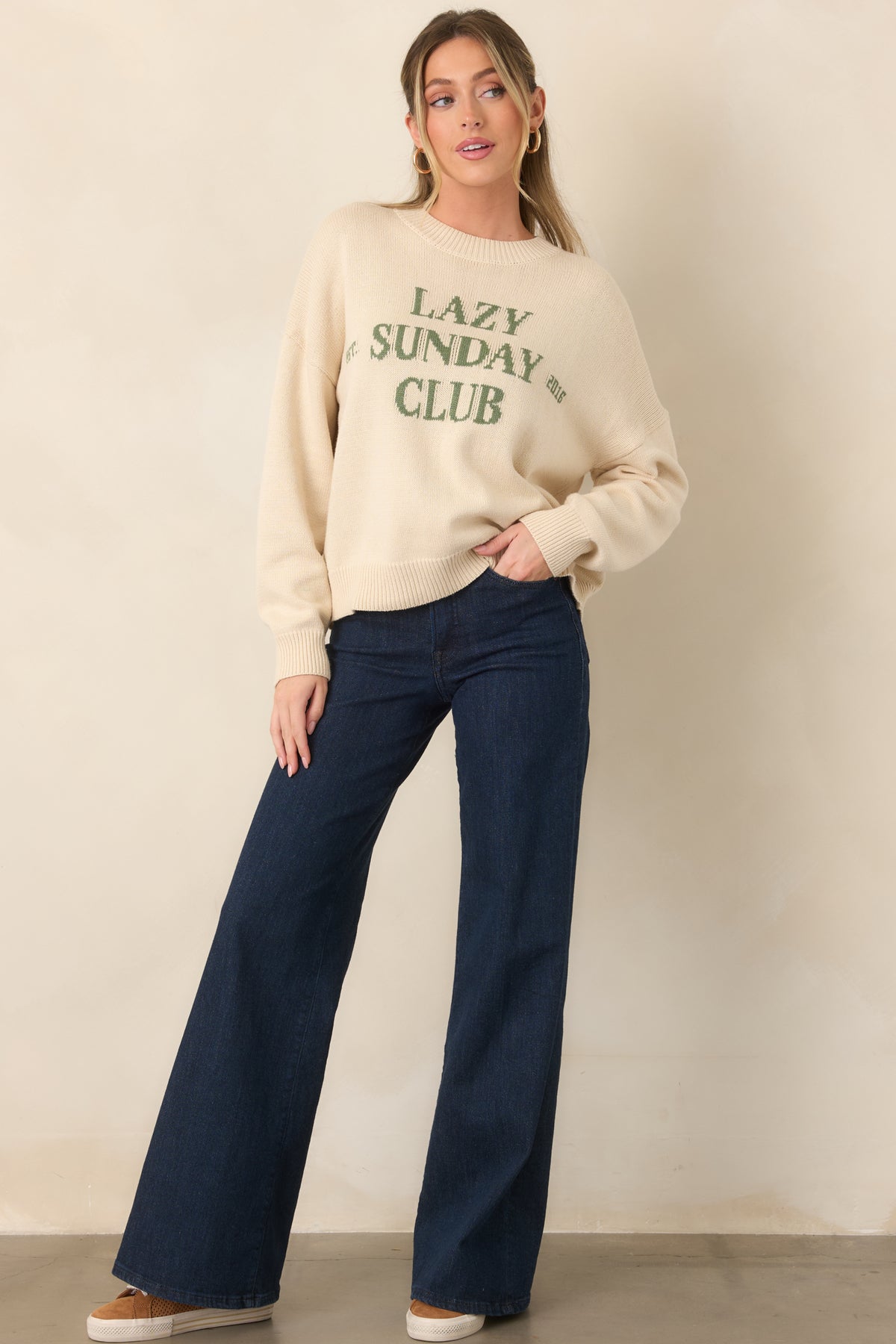 Soft ivory knit pullover designed with a classic crew neckline, relaxed fit, and contrasting green chest lettering.