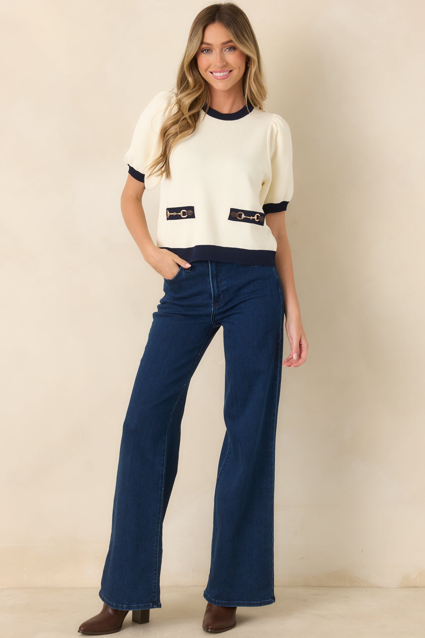 Ivory knit top featuring contrast navy ribbed trim, short puff sleeves, and gold-tone horsebit-style hardware.