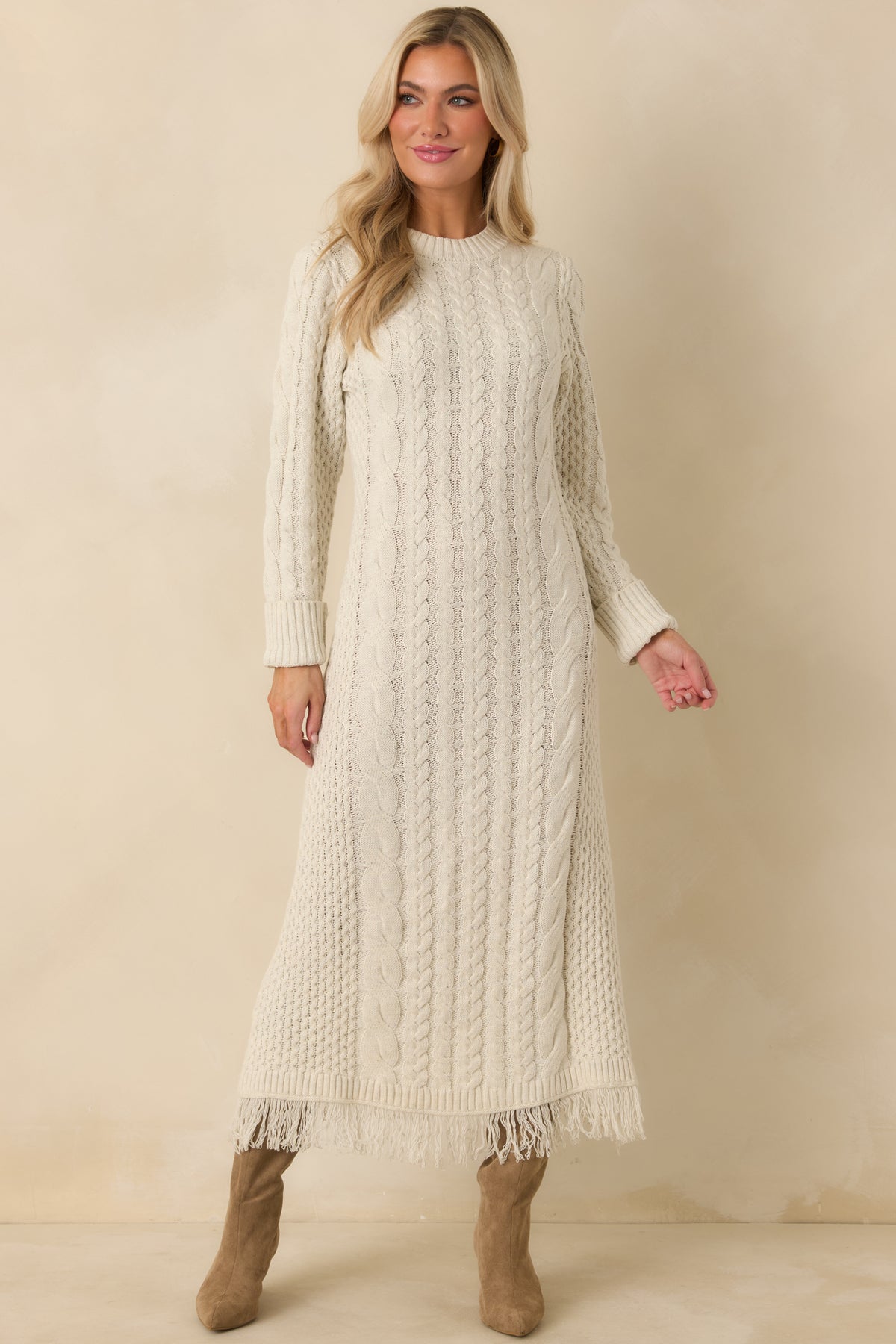 Ivory long sleeve sweater dress with allover cable knit texture, a crew neckline, and full-length fringed hem.