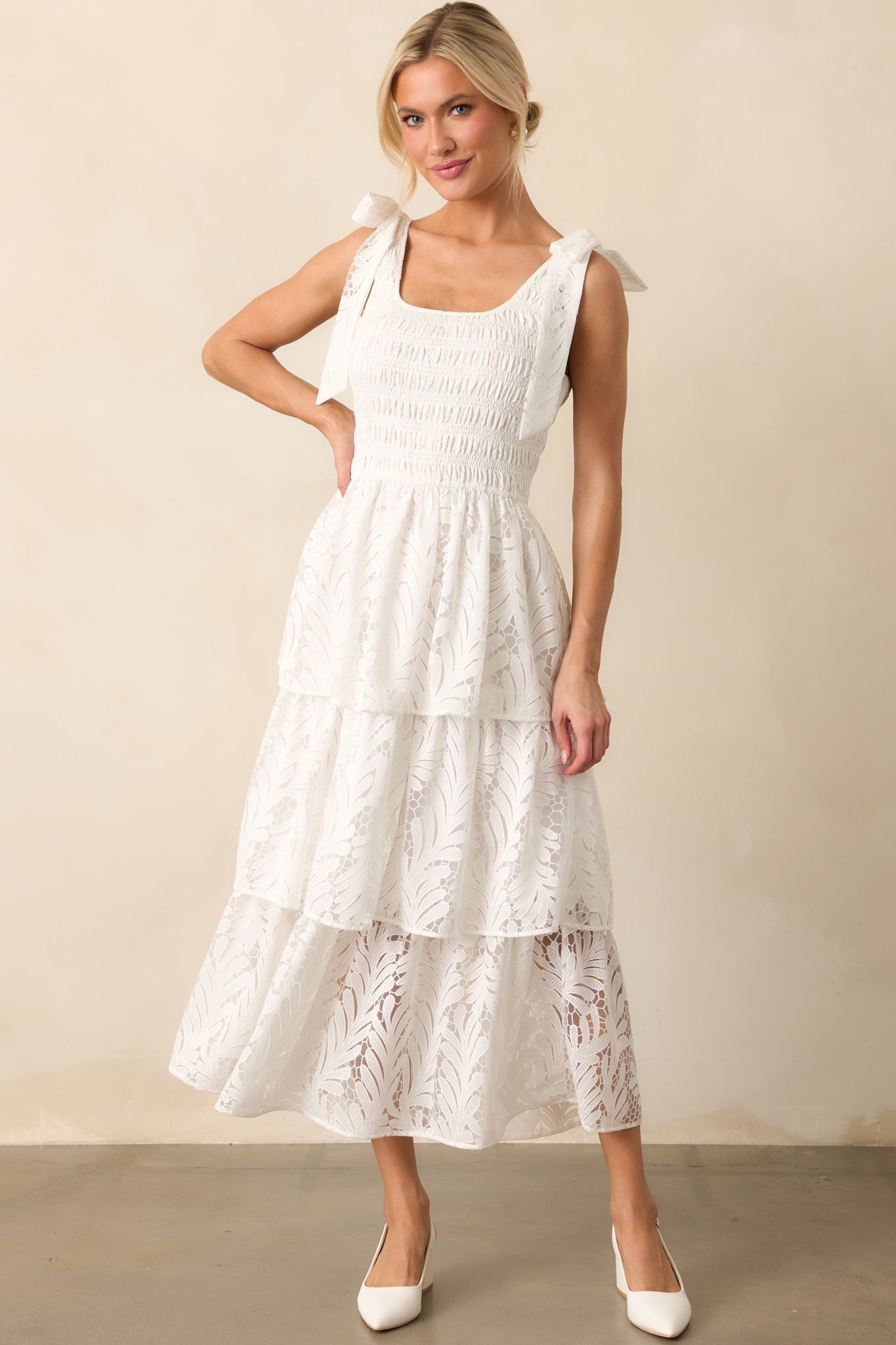 Ivory maxi dress with a scoop neckline, fully smocked bodice, and lace bow details on both shoulders, flowing into a tiered lace skirt.