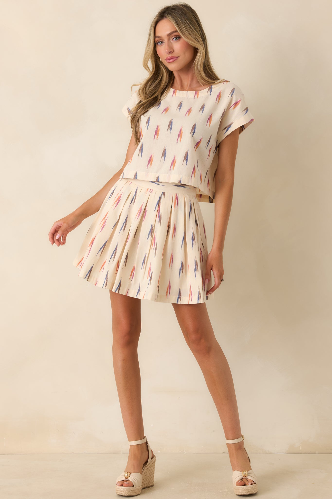 Ivory mini skirt with a colorful abstract print and pleated silhouette.