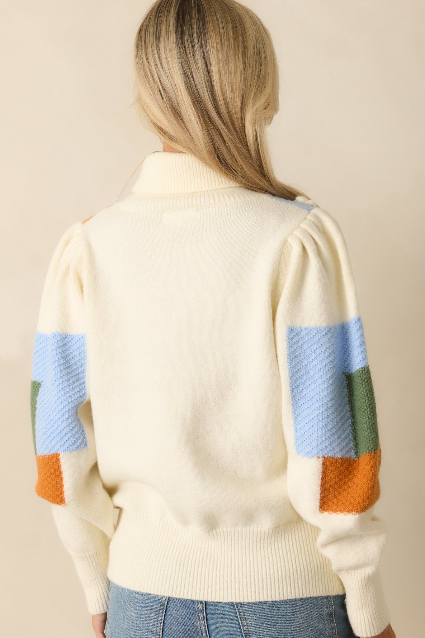 Rear view of the ivory multi-knit sweater showing ribbed hem, turtleneck, puff sleeves, and the patchwork colorblock design.
