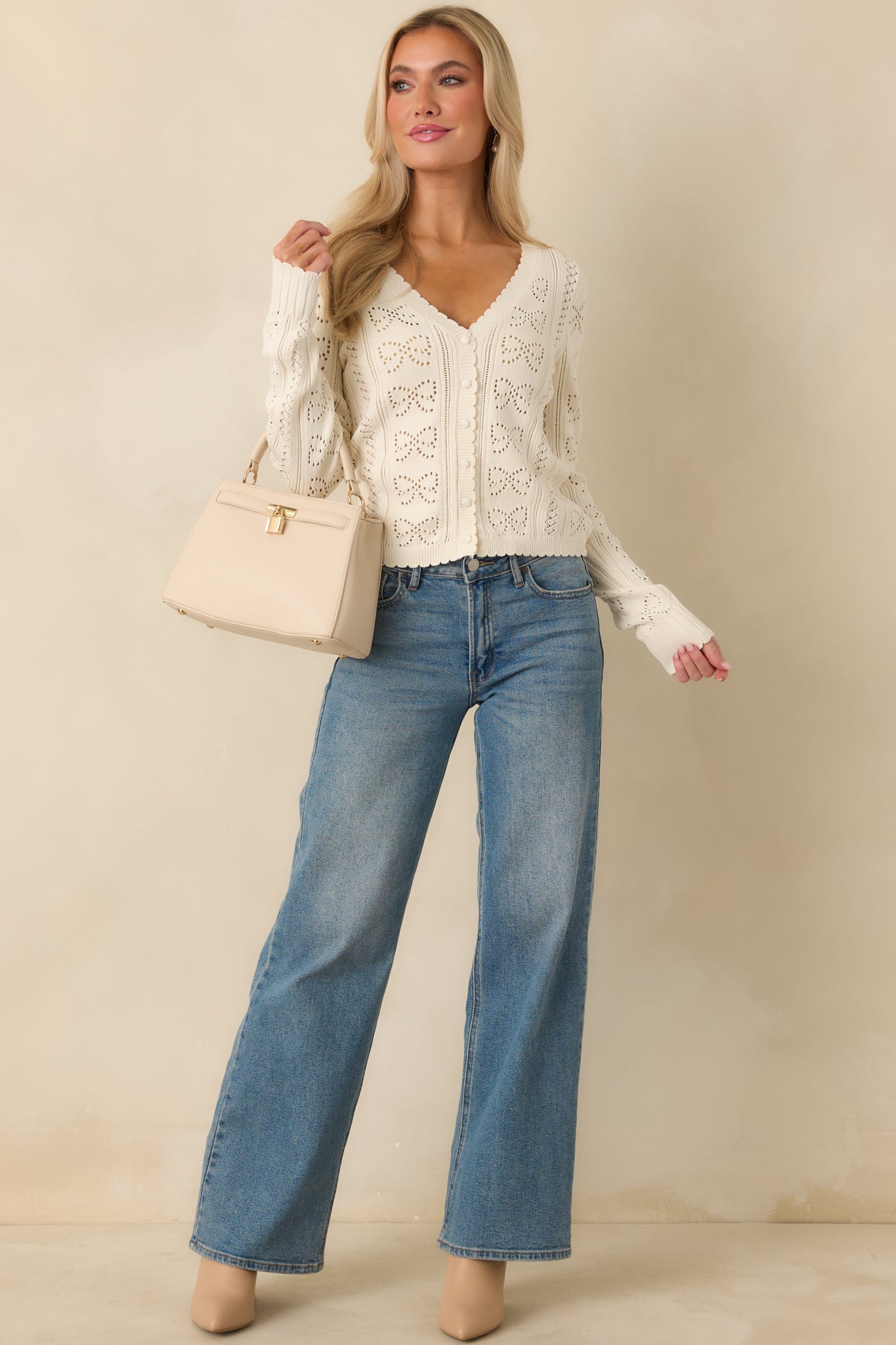 Ivory open-knit cardigan with a V-neckline, full button-front closure, and repeating bow motifs throughout.