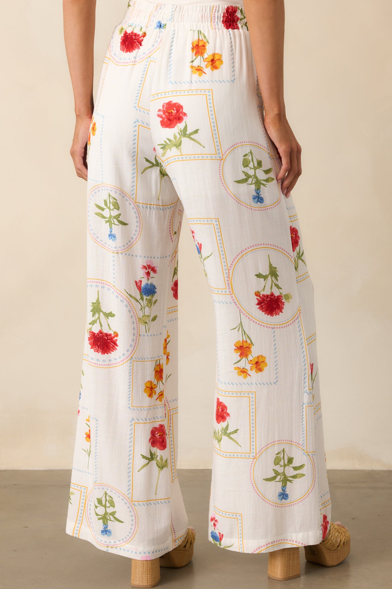 A back view showcasing the wide-leg silhouette and back detailing of the ivory pants with geometric floral patchwork.