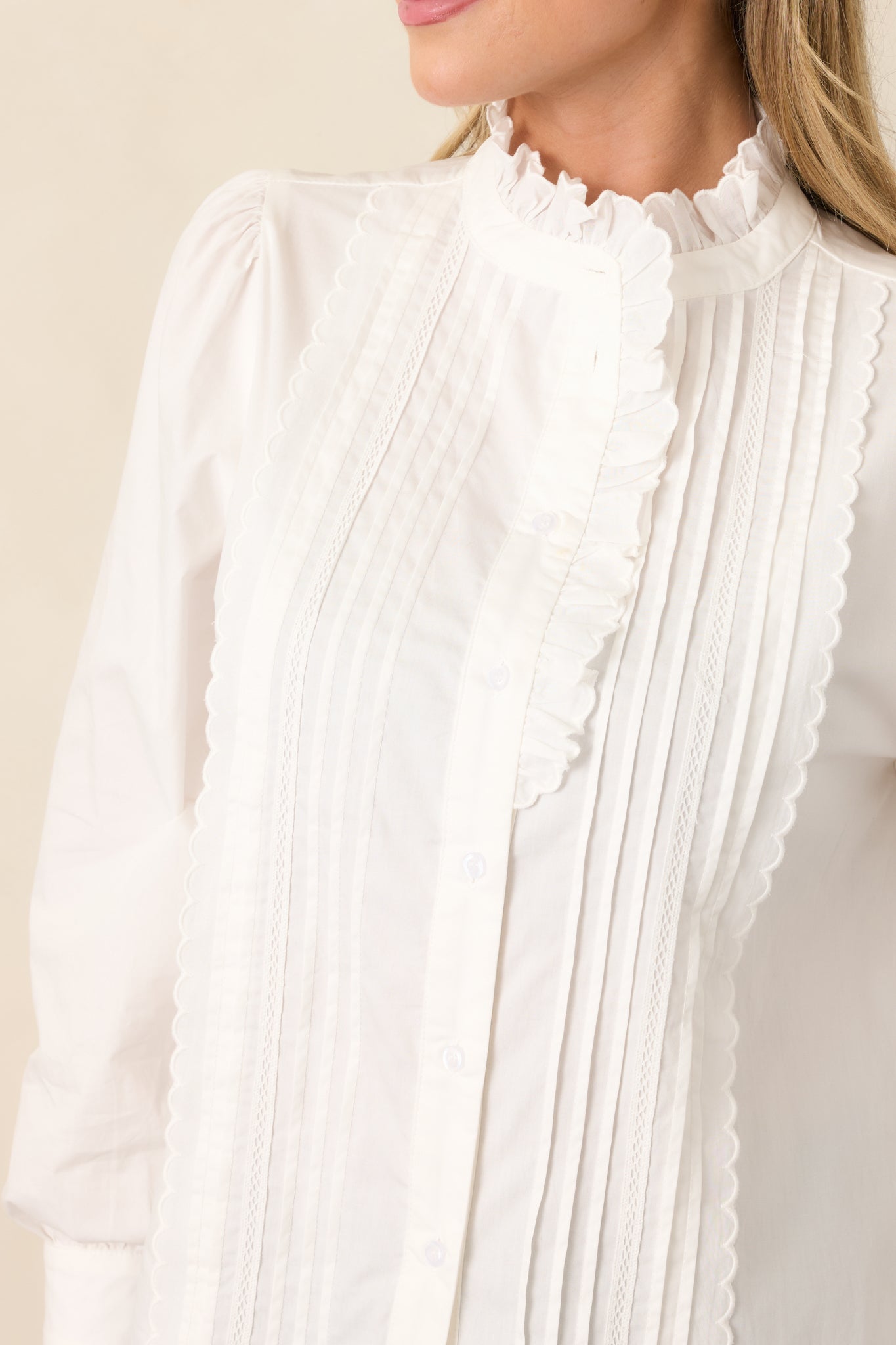 Detailed view highlighting the ivory pintuck detailing, ruffled high neckline, and delicate button-front construction.