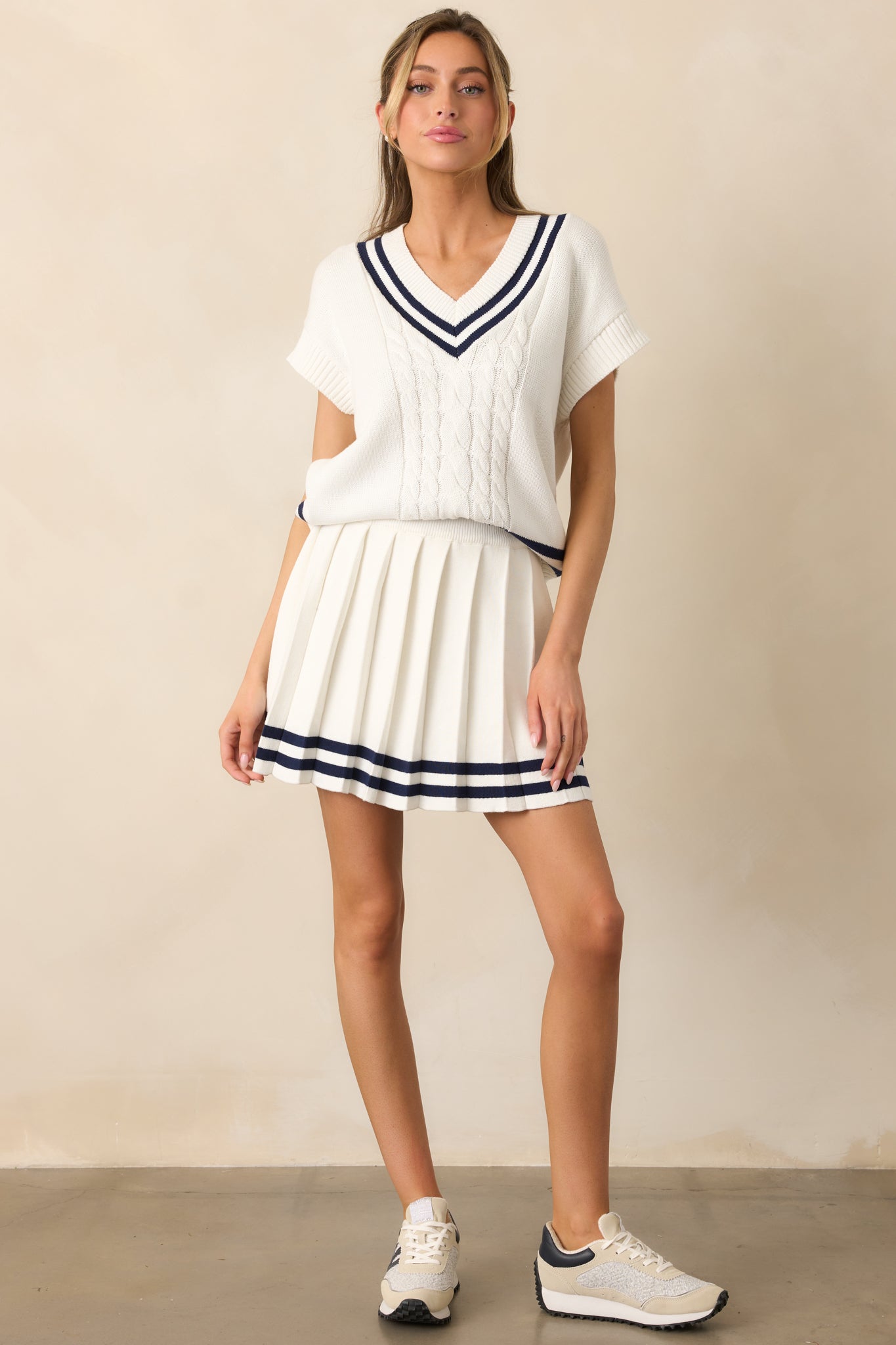 Ivory skirt with a pleated design, elastic waistband, and navy stripe detailing along the bottom hem, made from lightweight knit fabric with built-in stretchy shorts.