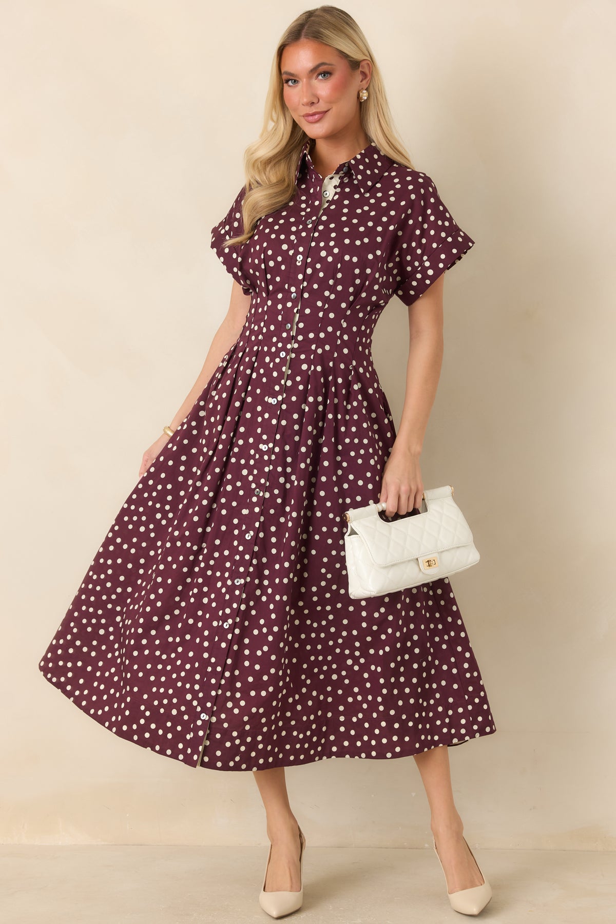 Ivory cotton midi dress with plum polka dots, collared neckline, button-front bodice, short sleeves, defined waist seams, and flowing fit-and-flare skirt.