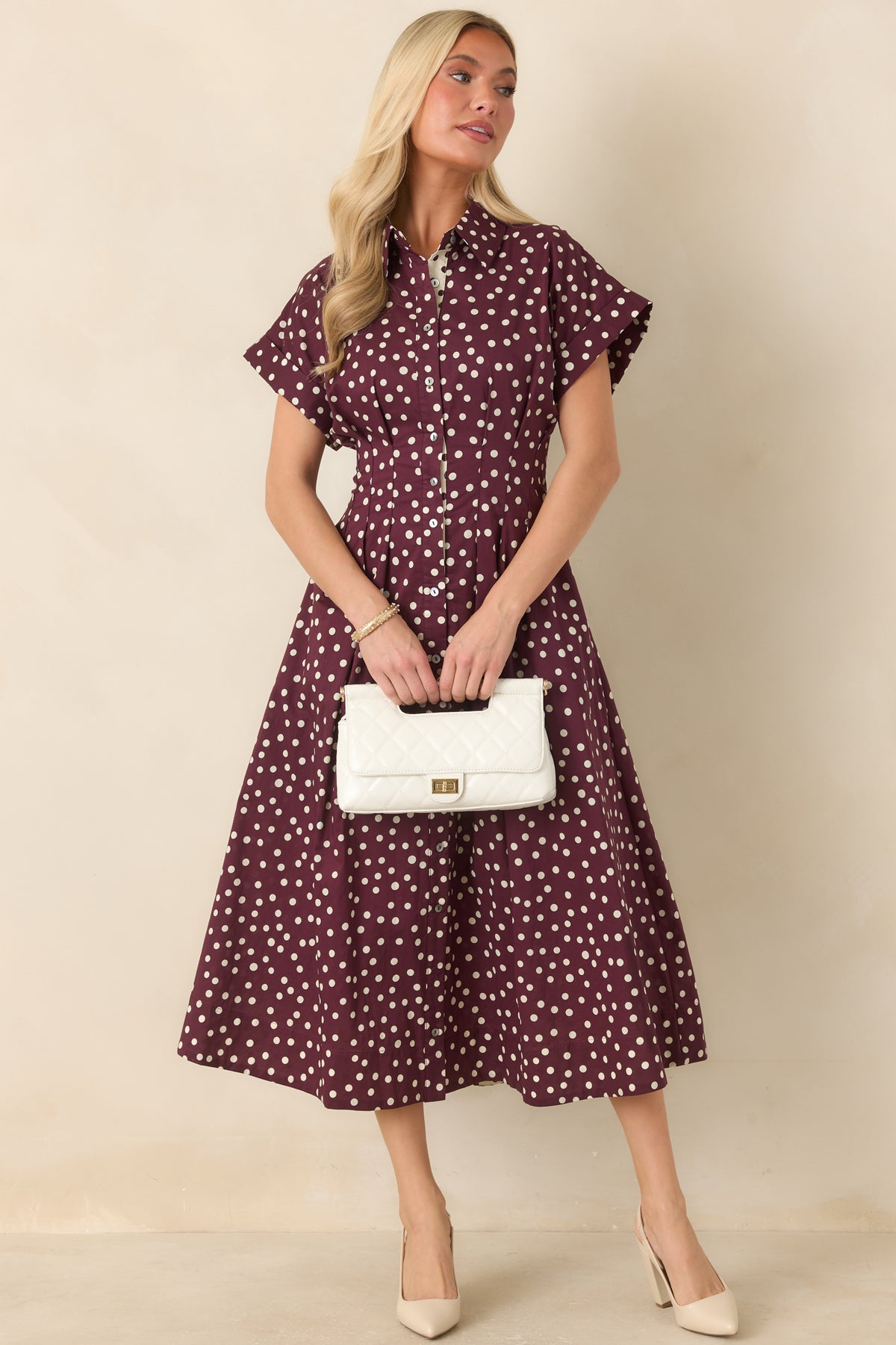 Ivory midi dress with plum polka dots, short sleeves, tailored waist seams, collared neckline, and a flowing skirt with side pockets