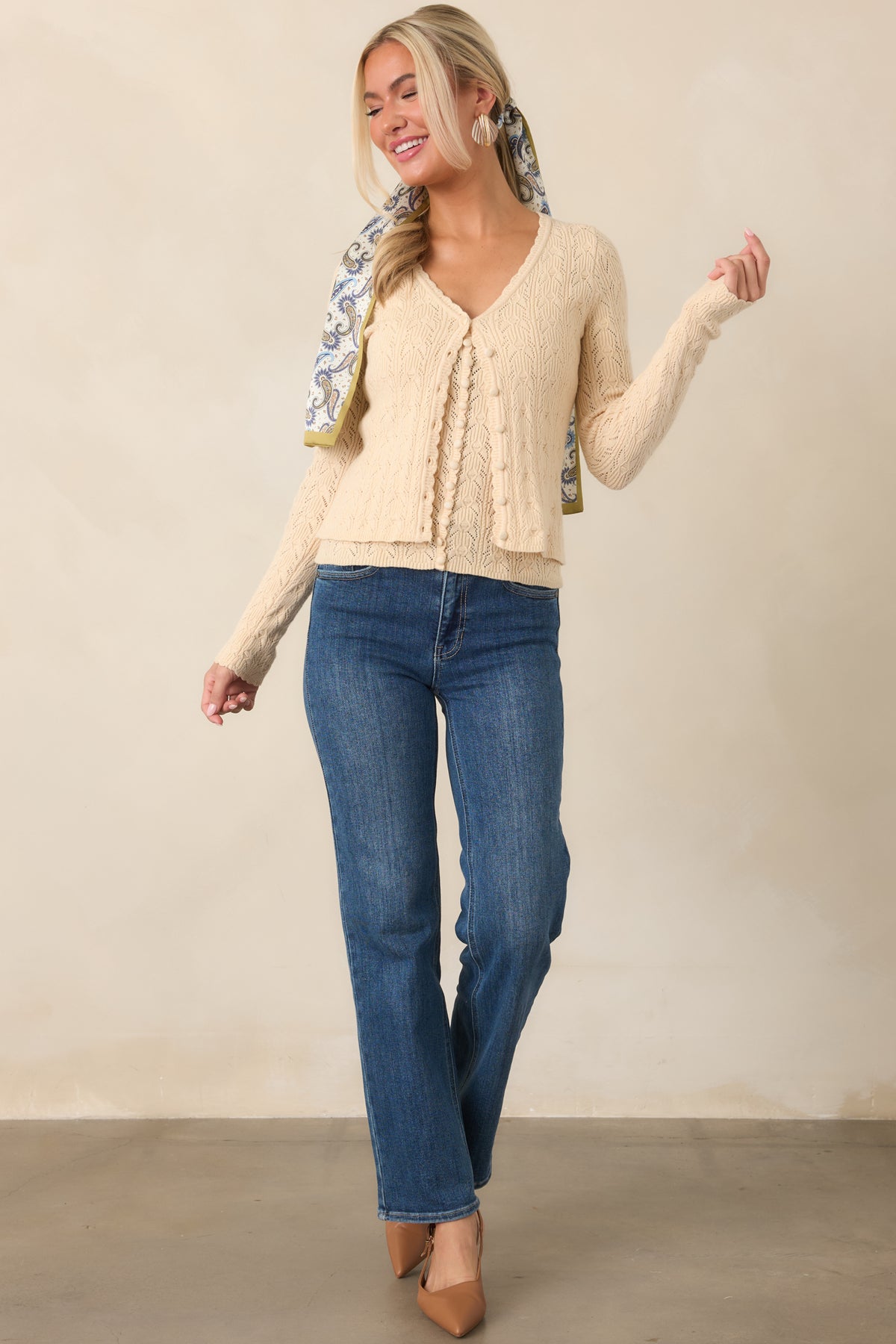 Soft ivory knit cardigan designed with an openwork pointelle pattern, scalloped neckline, long sleeves, and a functional button closure.