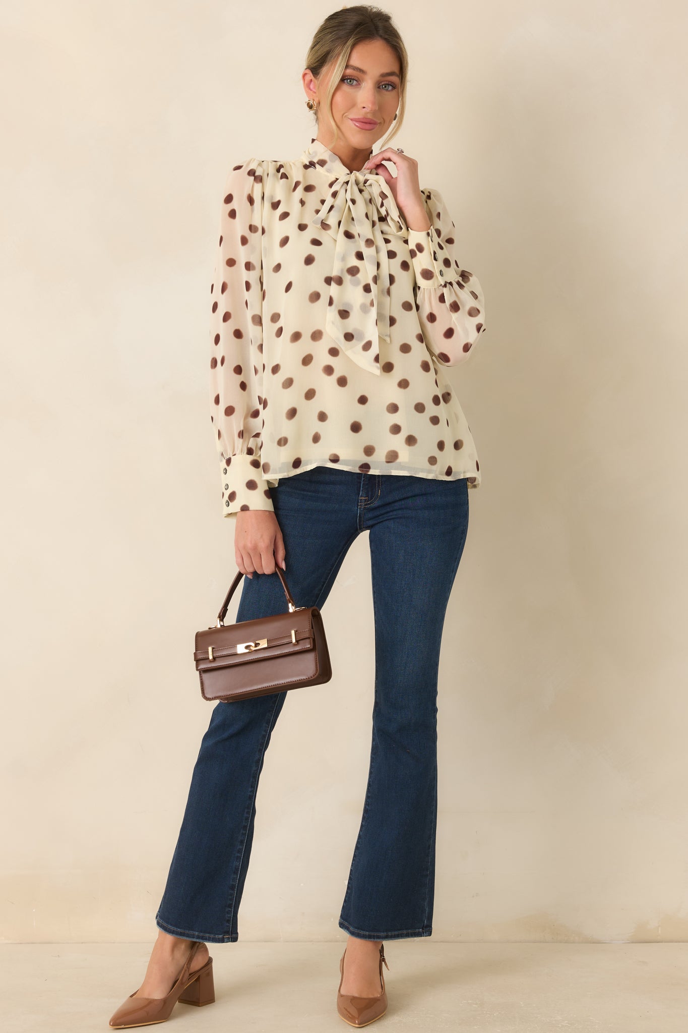 Ivory polka dot chiffon blouse featuring a feminine tie neckline, soft shoulder gathering, and elegant long sleeve silhouette.