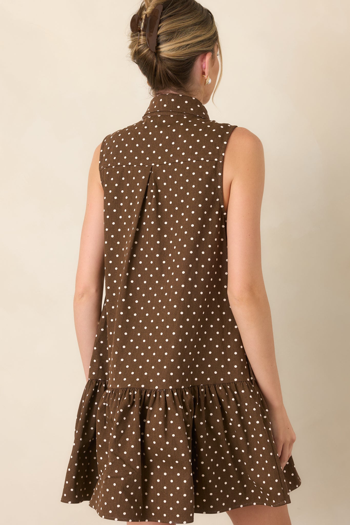 Rear view of the ivory polka dot mini dress, highlighting its sleeveless silhouette, relaxed drop waist, and gathered ruffle hem.