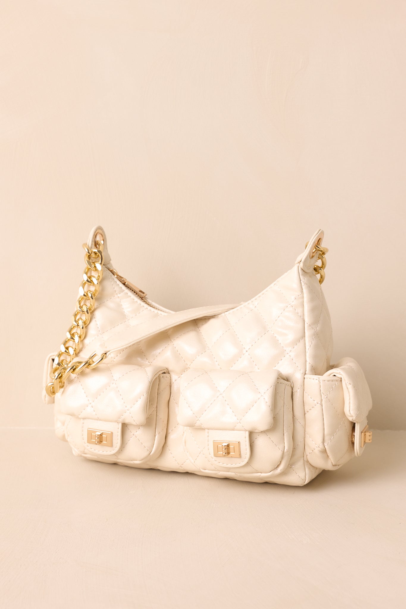 A full view of the ivory quilted handbag showing the structured silhouette and gold chain shoulder strap.