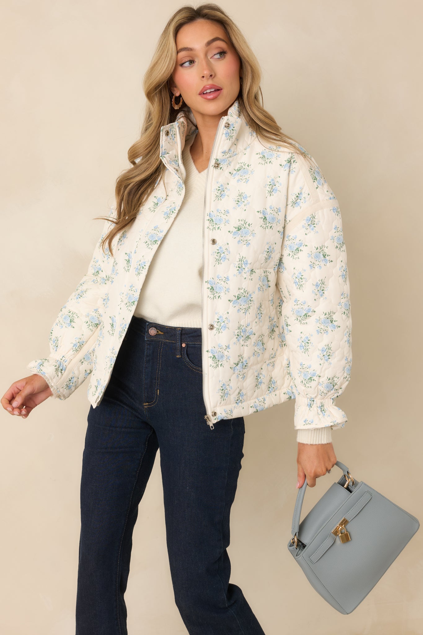 Ivory quilted jacket with allover blue floral print, high neckline, long sleeves, front pockets, and snap-button closure for easy wear.