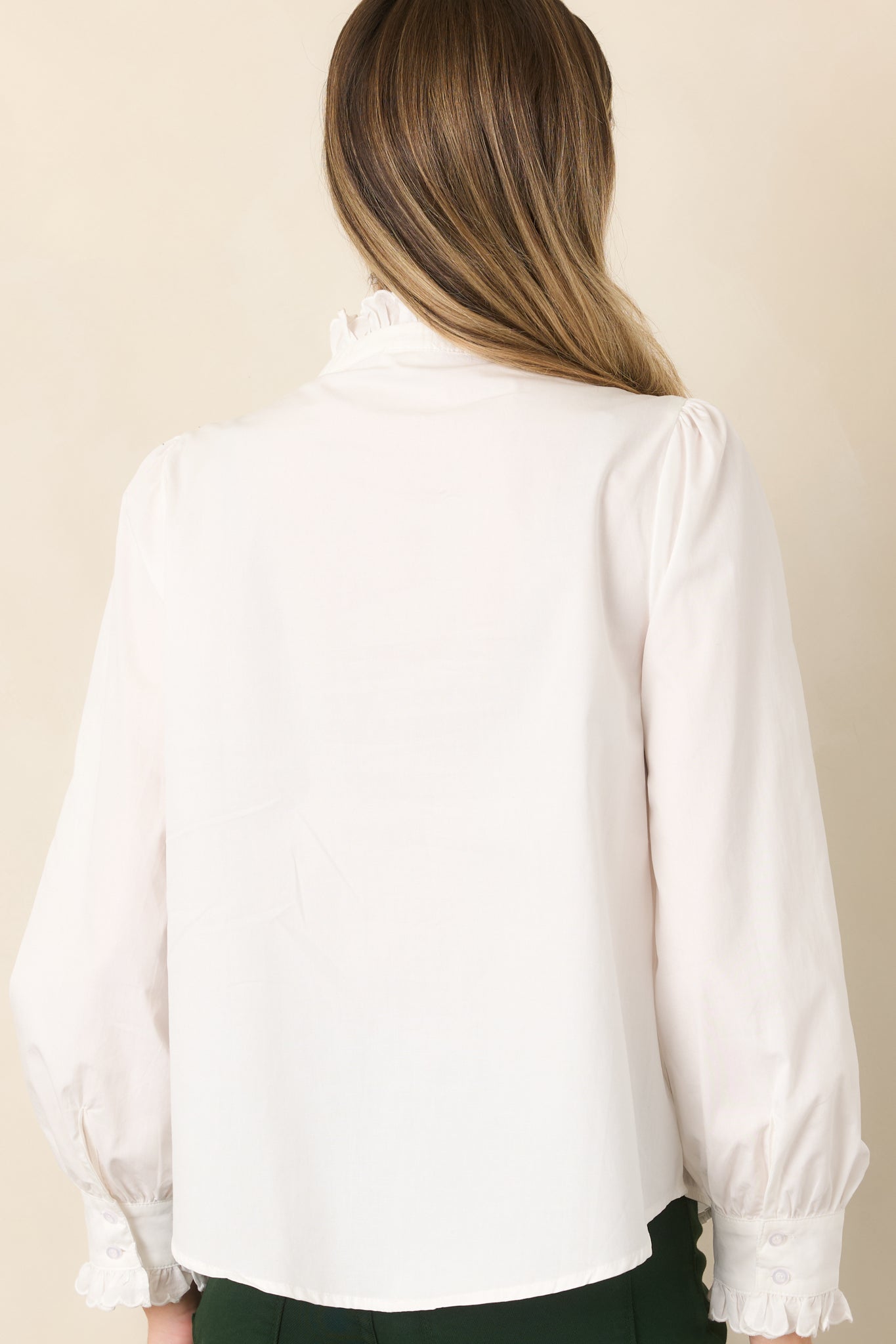 Rear view of the ivory blouse showcasing its relaxed silhouette, ruffle-trimmed shoulders, long sleeves, and softly gathered cuffs.
