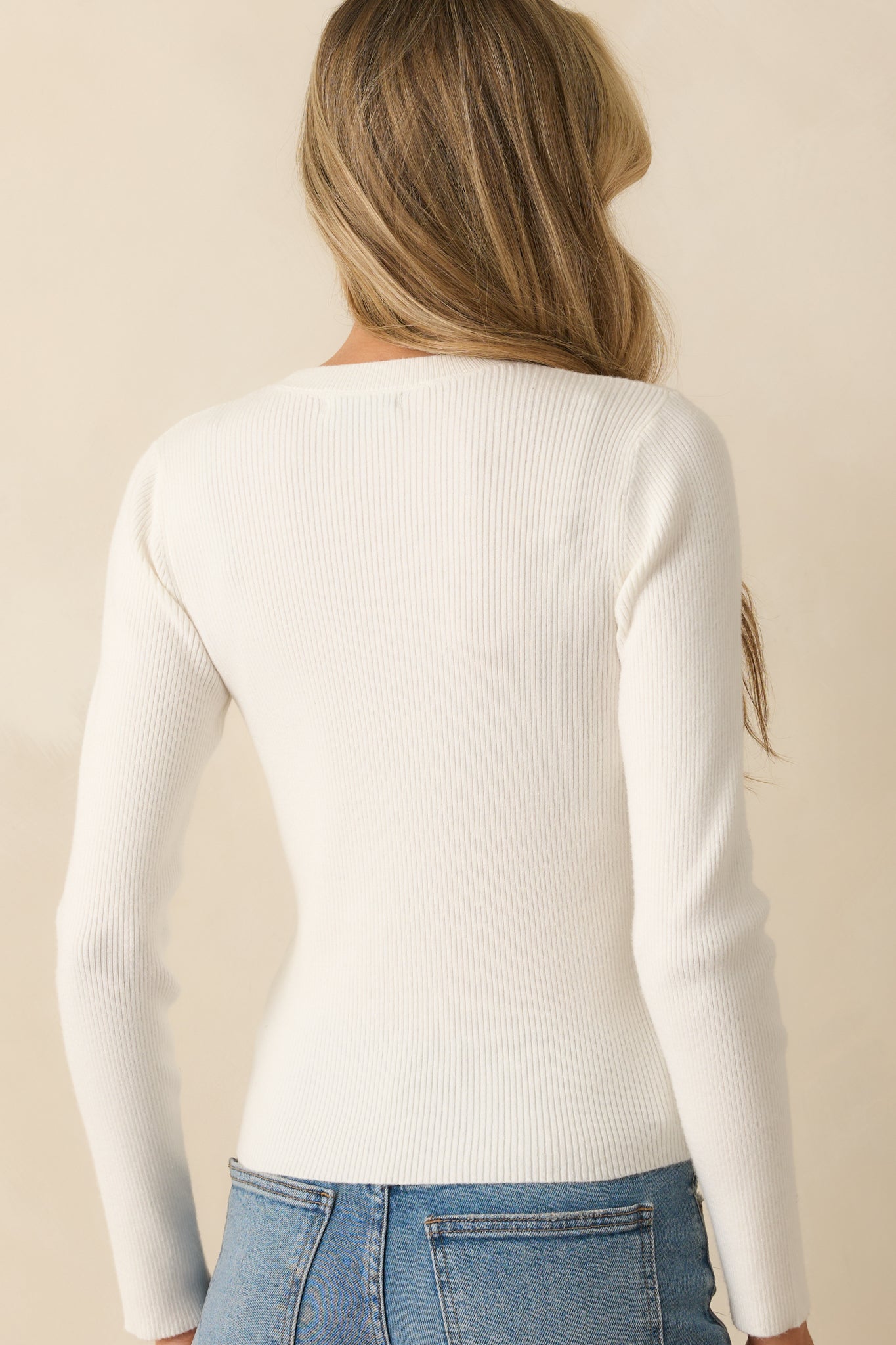 Rear view of ivory ribbed sweater with long sleeves, fitted shape, and straight hem.