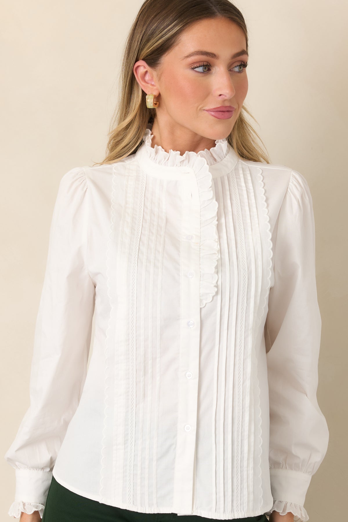 Close view of the ivory blouse highlighting the ruffled high neckline, vertical pintucks, and functional button-front closure.