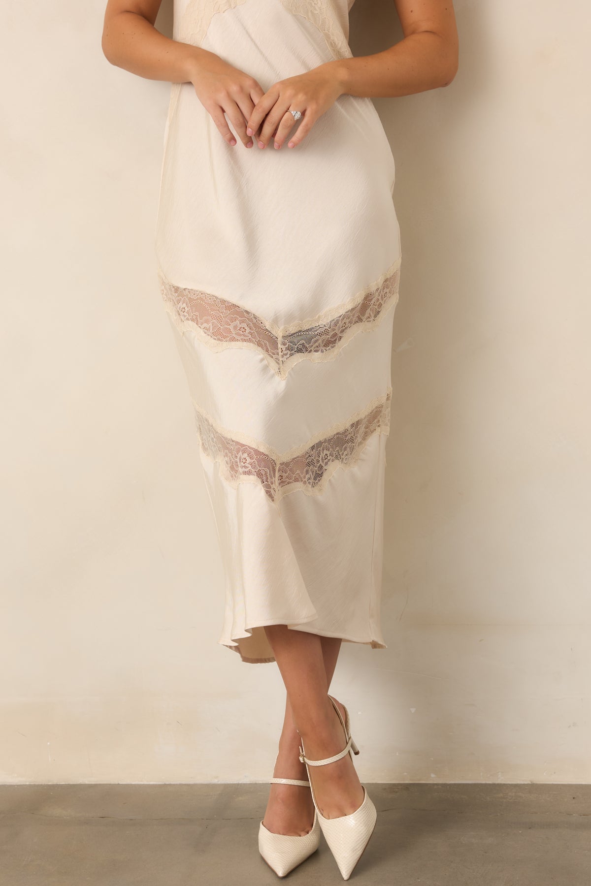 Close-up of the ivory satin dress showing the crinkled texture and angled lace detailing along the bottom hem.