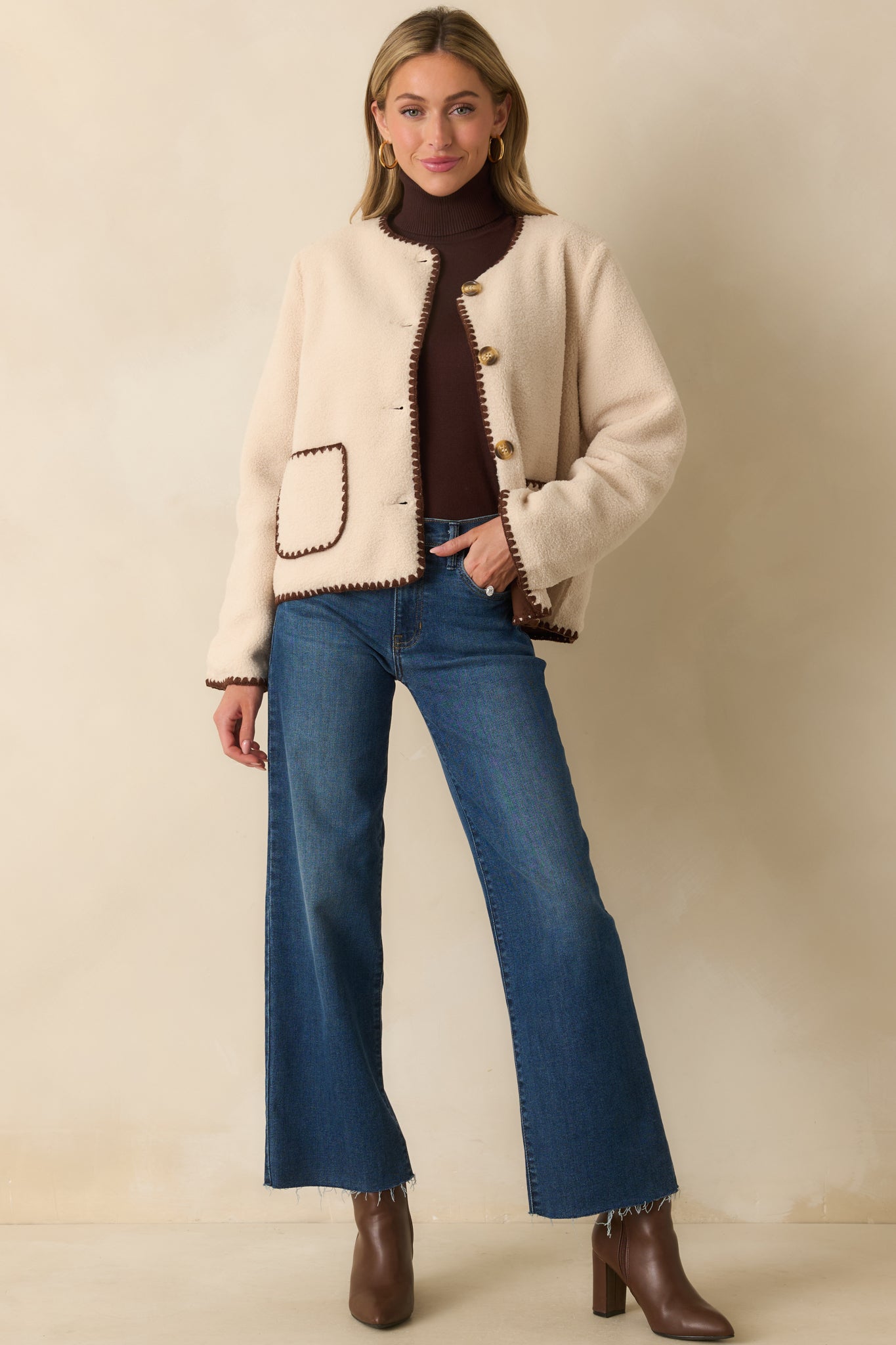 Ivory sherpa fleece jacket with a slightly cropped boxy fit, tortoise shell button front, and chocolate brown whipstitch trim.