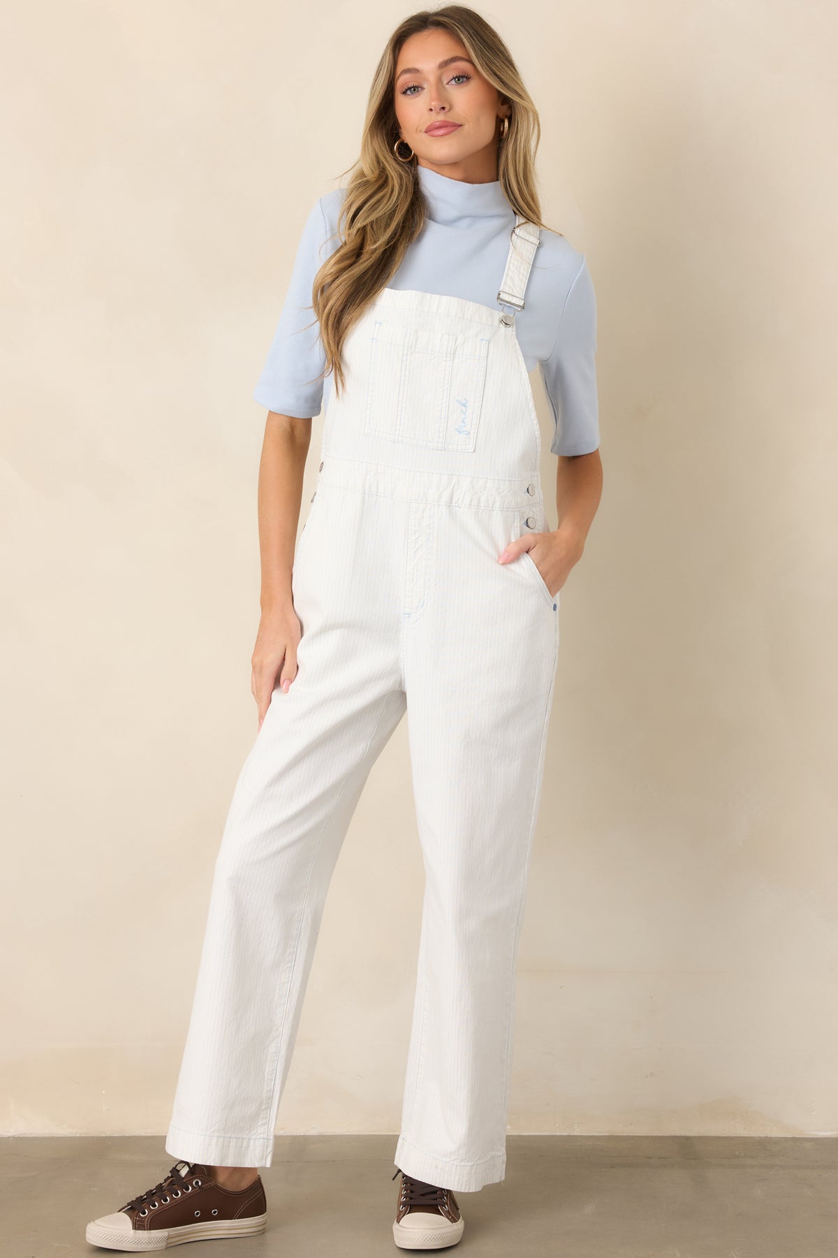 Ivory and sky blue cotton jumpsuit showcasing cross-back straps with buckle closures, a chest pocket, side buttons, and cropped straight legs.