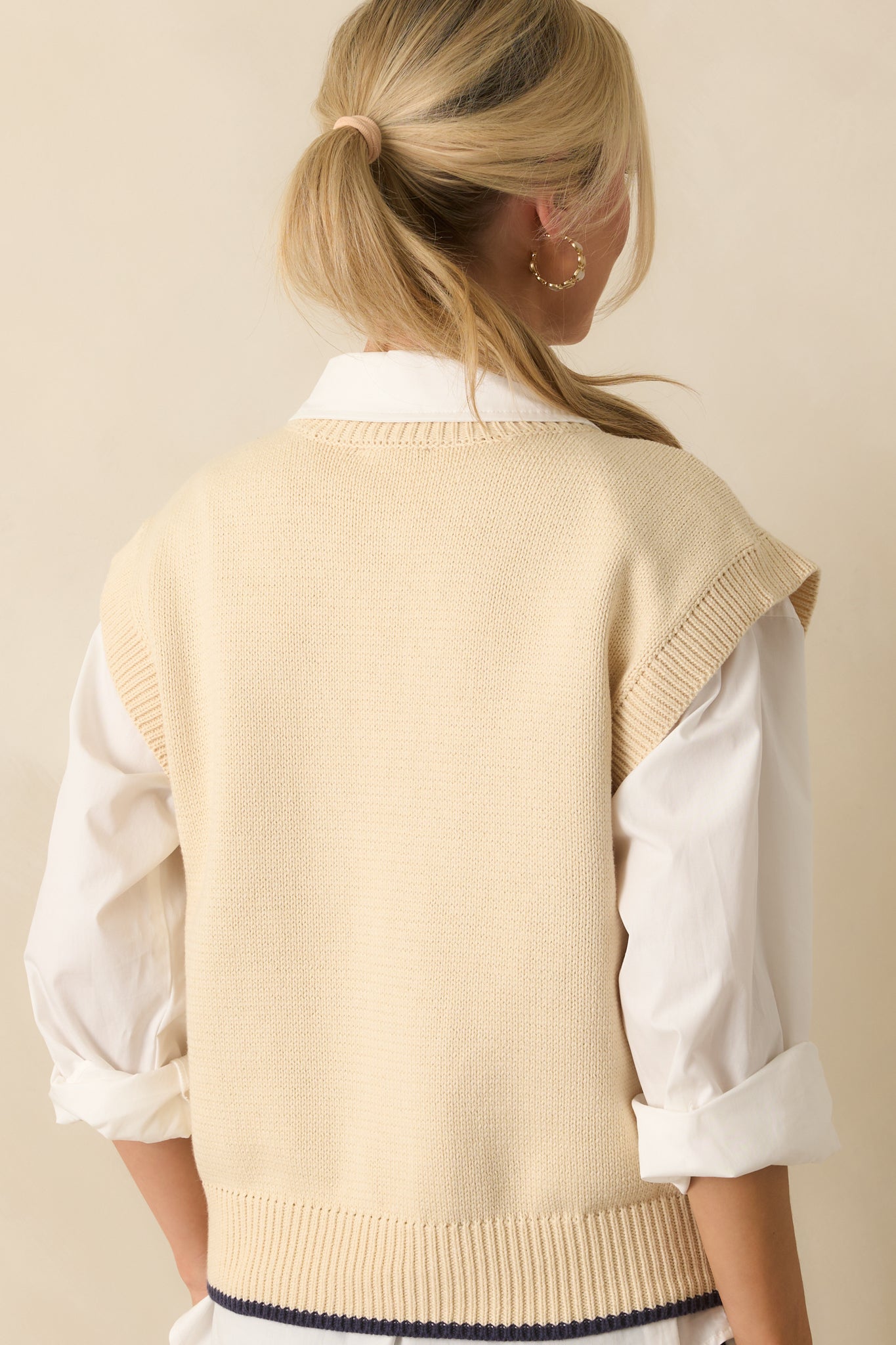 Rear view of the ivory sleeveless vest showing clean knit fabric and ribbed hem.
