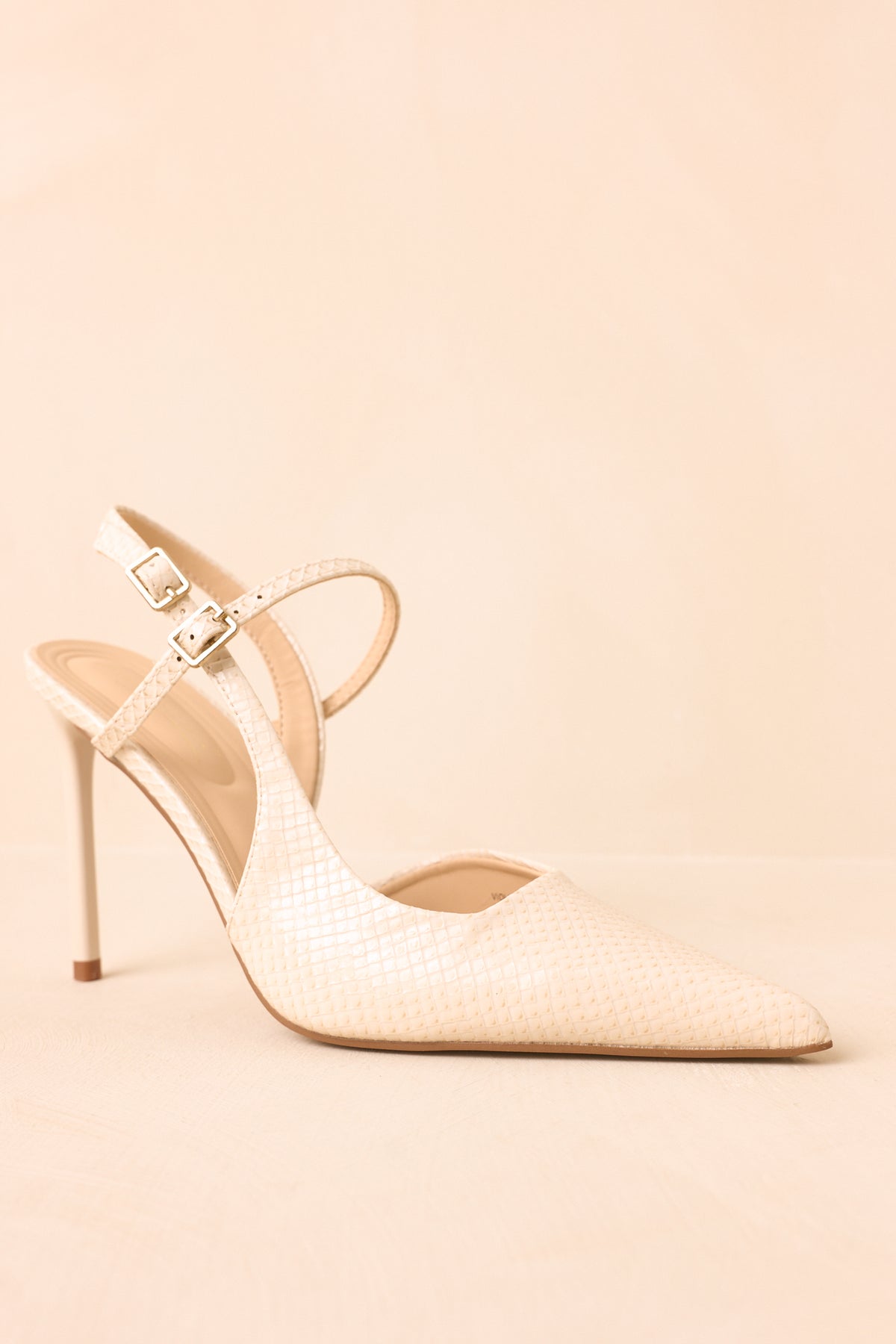 Ivory slingback heels highlight a feminine pointed toe, slender stiletto heel, and petite buckle closures along the double straps.