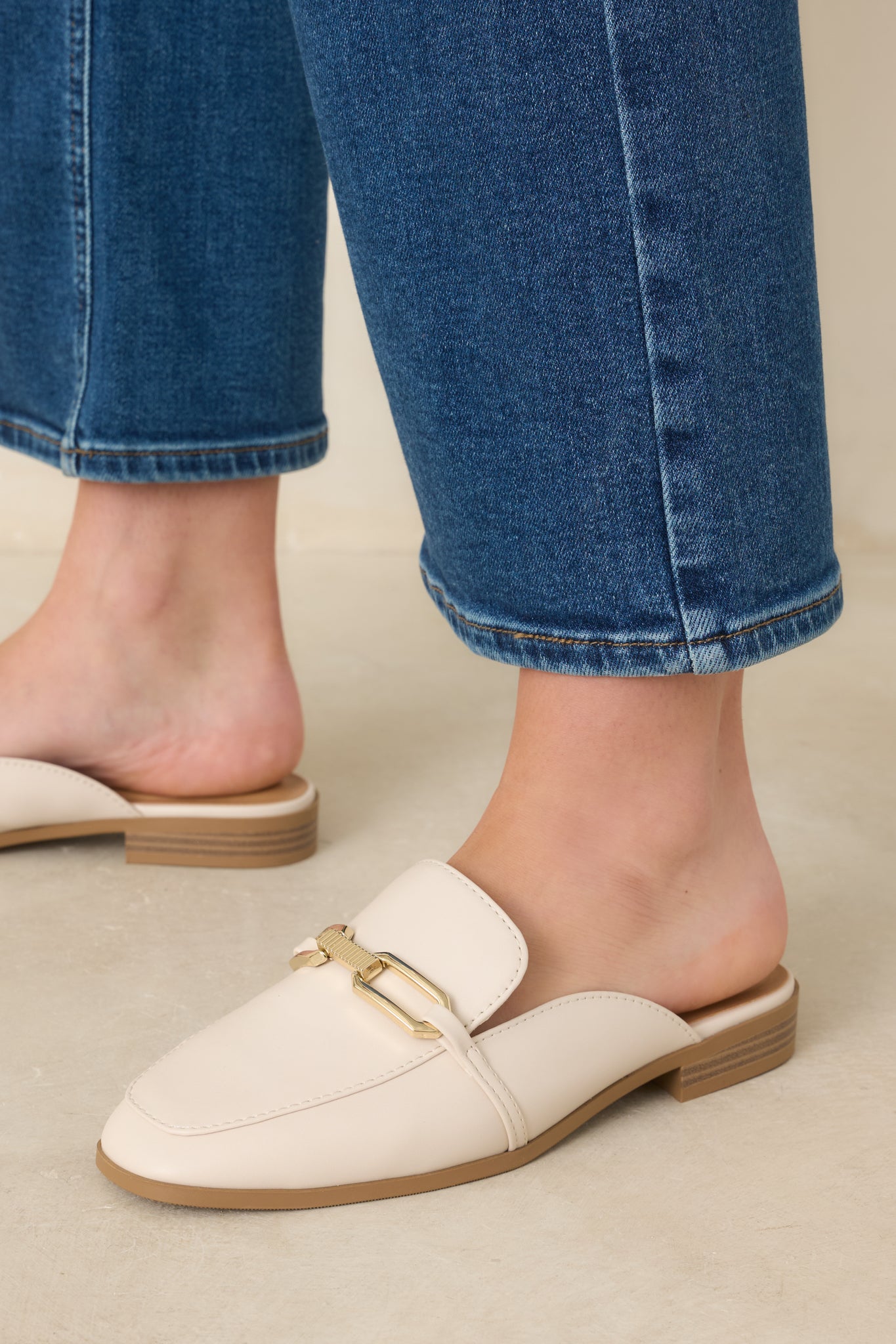 Cropped front view of ivory slip-on mule loafers featuring almond toe silhouette and gold-tone hardware bit.