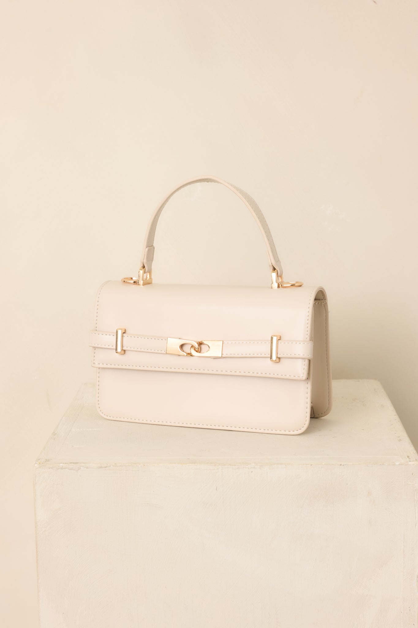 Soft ivory structured handbag featuring polished gold-tone hardware, an elegant front belt detail, top handle, and detachable shoulder strap.