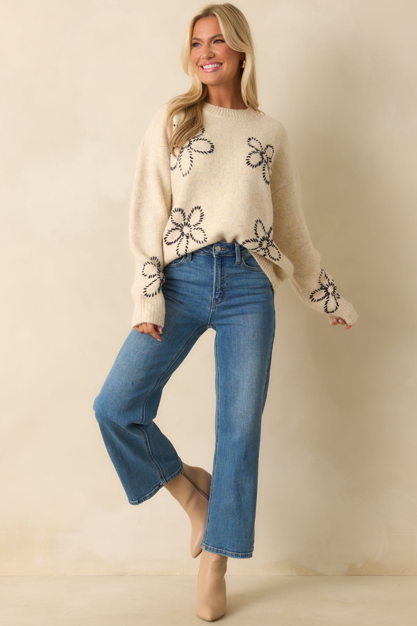 Ivory sweater with black embroidered floral motifs, classic crew neckline, and long sleeves with ribbed hems.