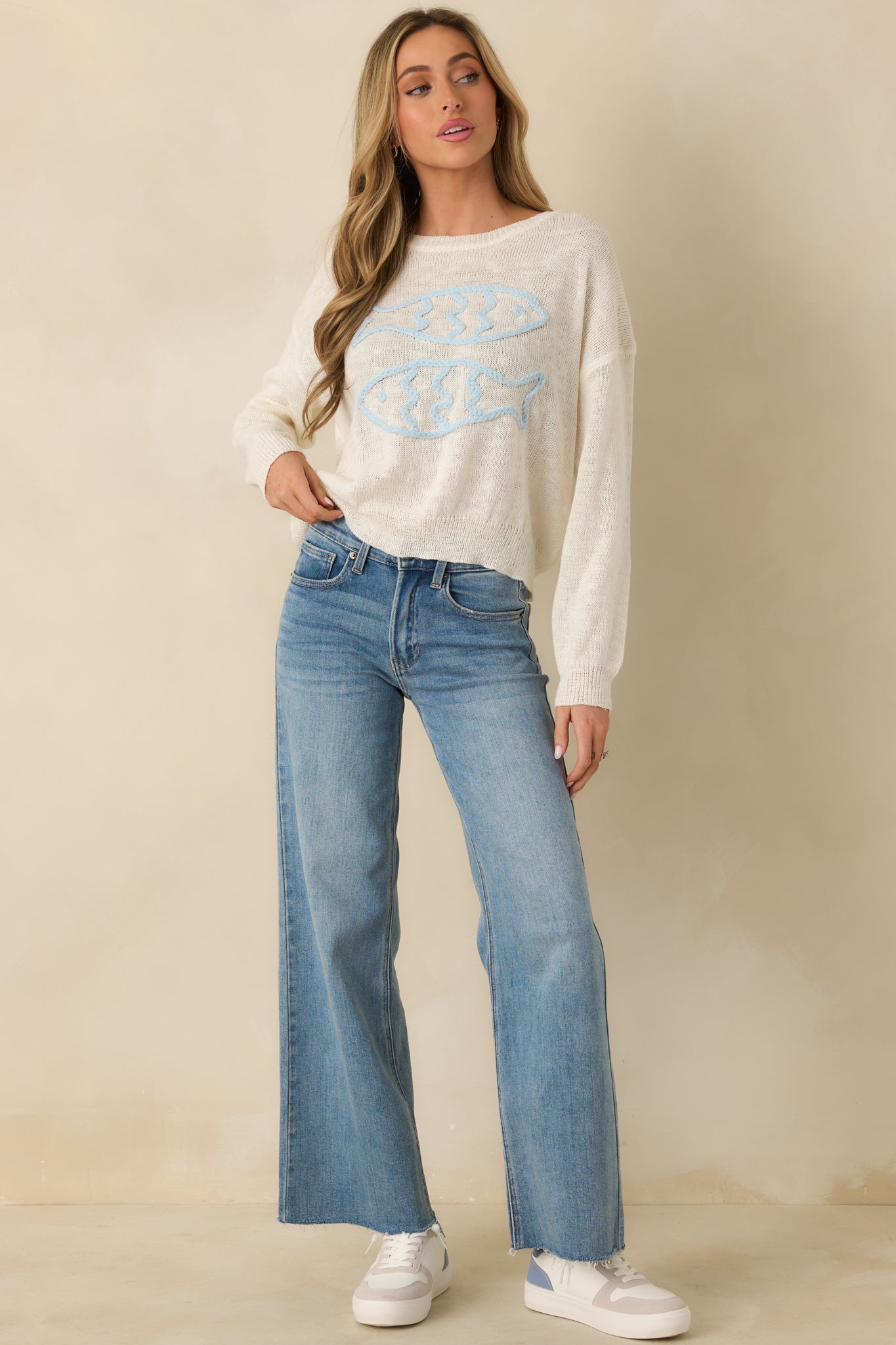 Front-facing ivory sweater featuring soft blue embroidered fish motifs and casual silhouette.