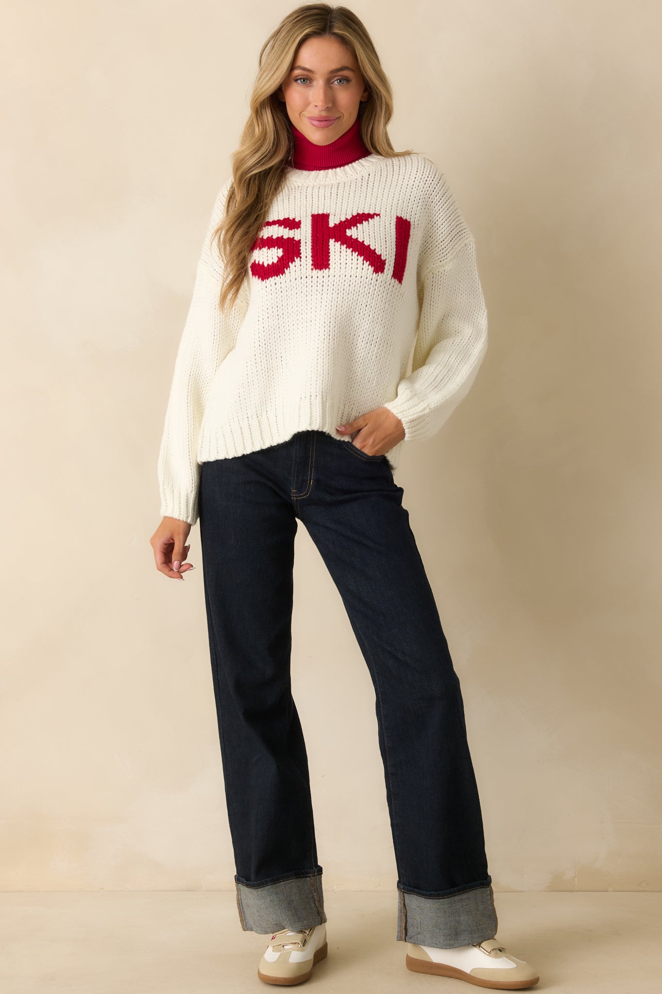 Front view showing the ivory sweater’s ribbed hem, cuffs, and bold “SKI” text.