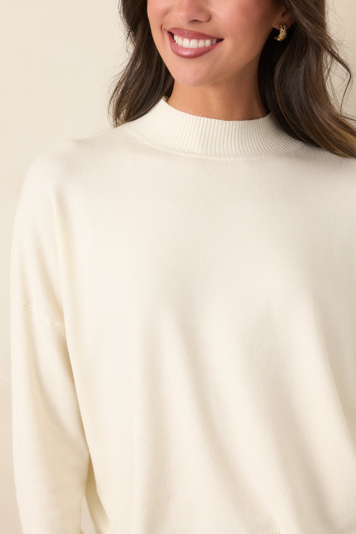 Close-up of the ivory sweater's smooth knit fabric and ribbed mock neckline, highlighting the contrasting knit textures.