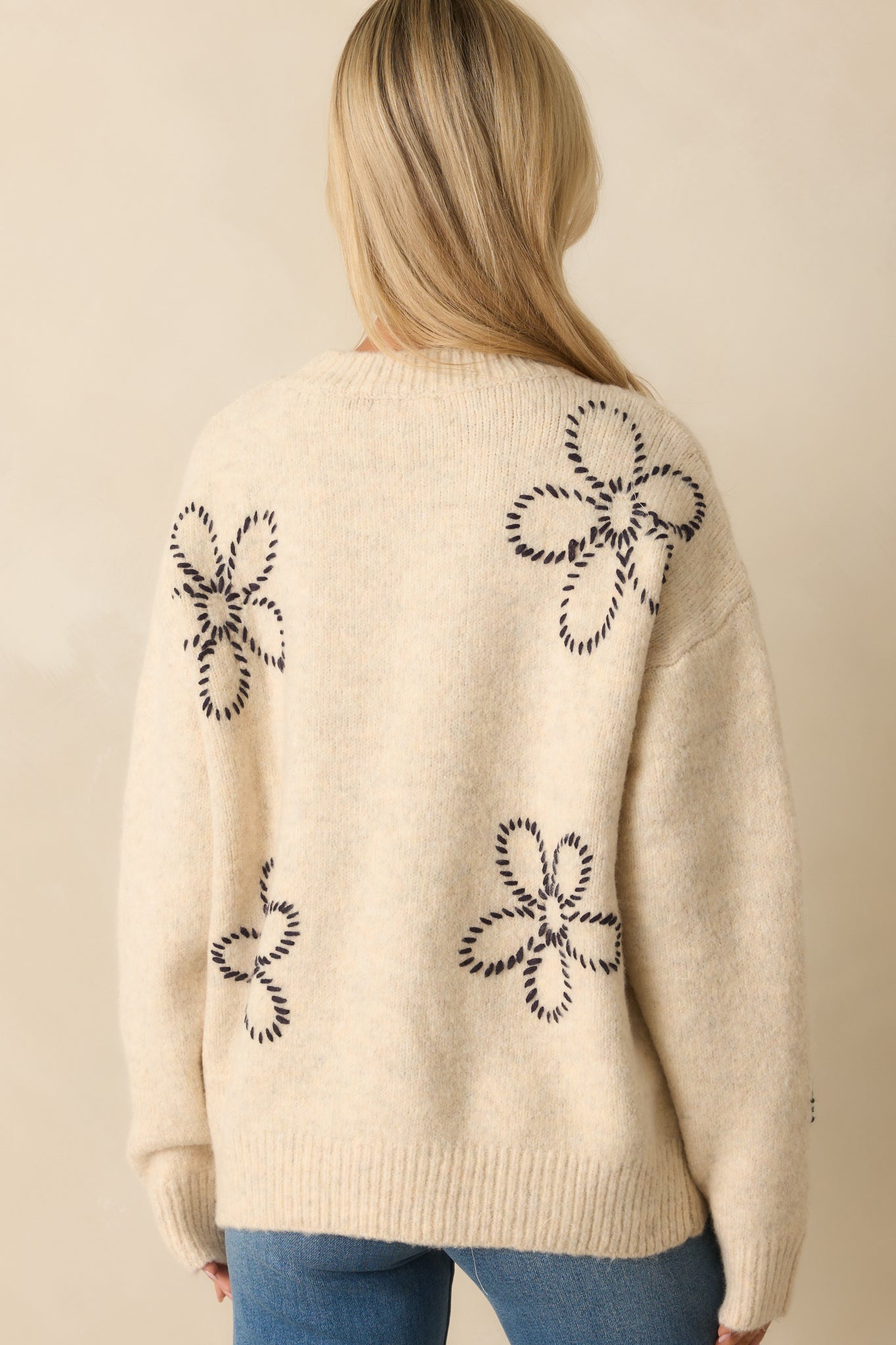 Rear view of the ivory sweater showing long sleeves, ribbed hems, and black floral embroidery across the back.