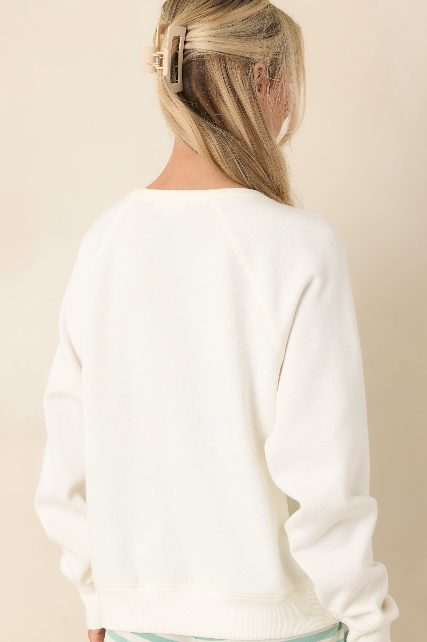 Rear view of ivory sweatshirt featuring raglan sleeves and a clean, unembellished finish with ribbed hem and cuffs.