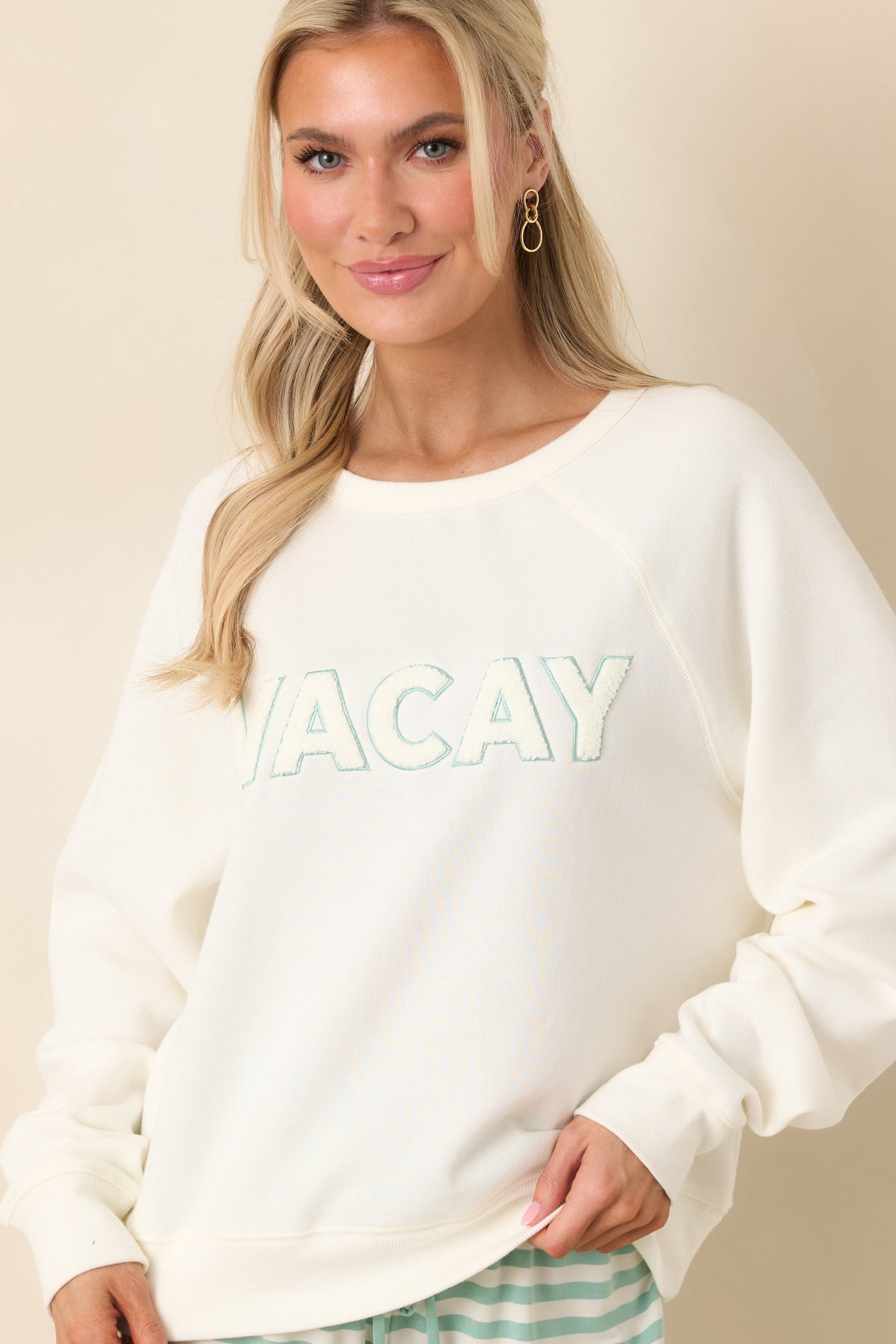 Textured “VACAY” applique lettering adding subtle contrast against the smooth ivory sweatshirt material.