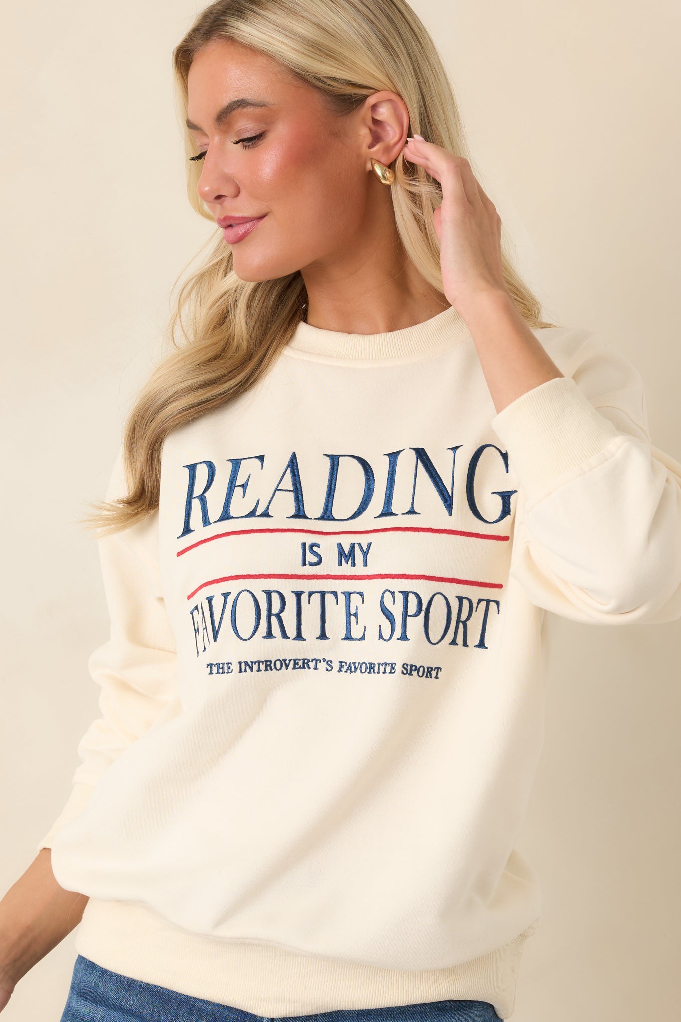 The front of this ivory sweatshirt highlights the embroidered “Reading Is My Favorite Sport” phrase and crew neckline.