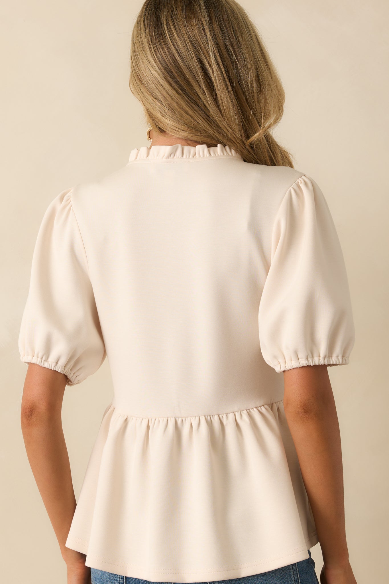 Rear view of ivory top showing short puff sleeves with elastic cuffs and the peplum hem.